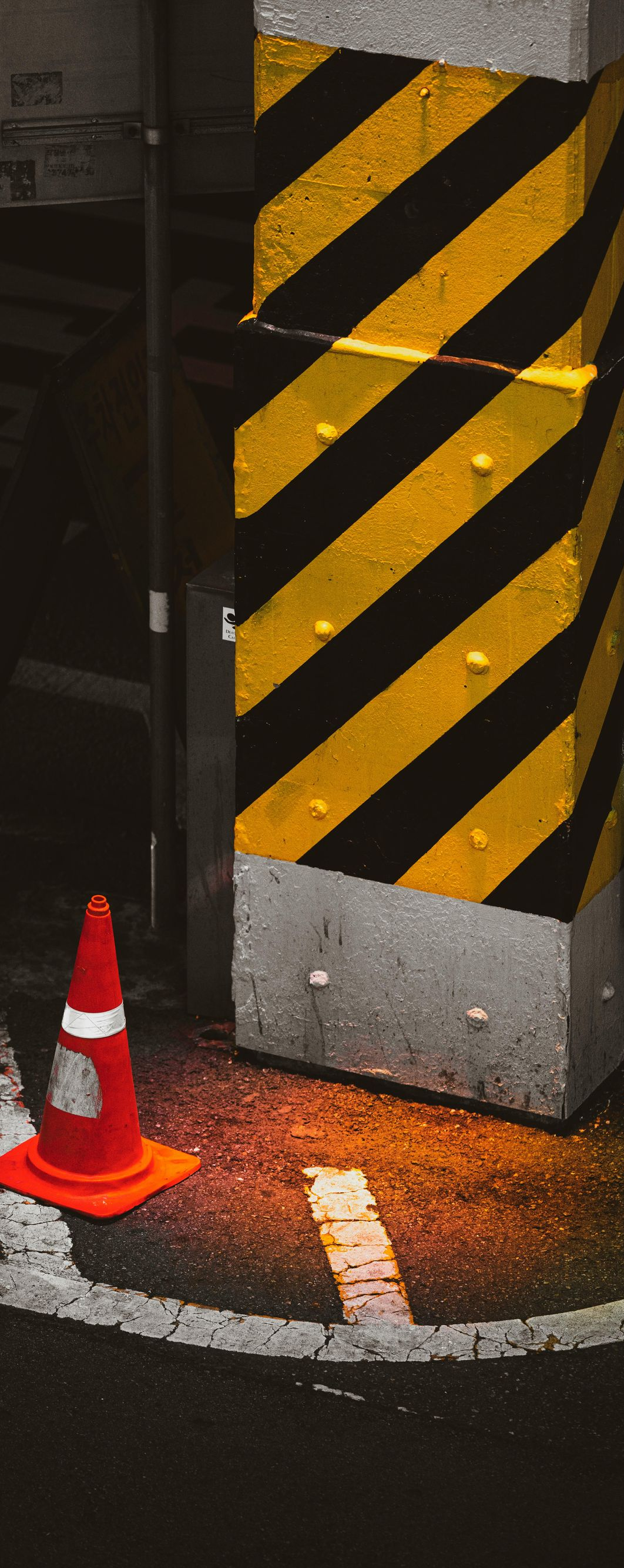 Black-and-yellow striped pillar with orange traffic cone at its base in a dim parking area