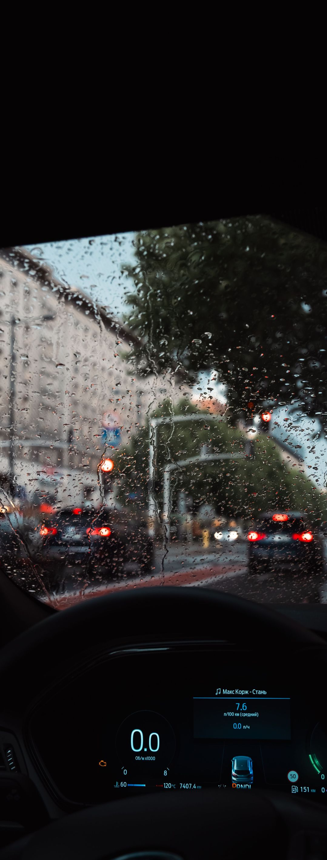 Rainy street view from a car, with traffic lights, wet road, and dashboard visible.