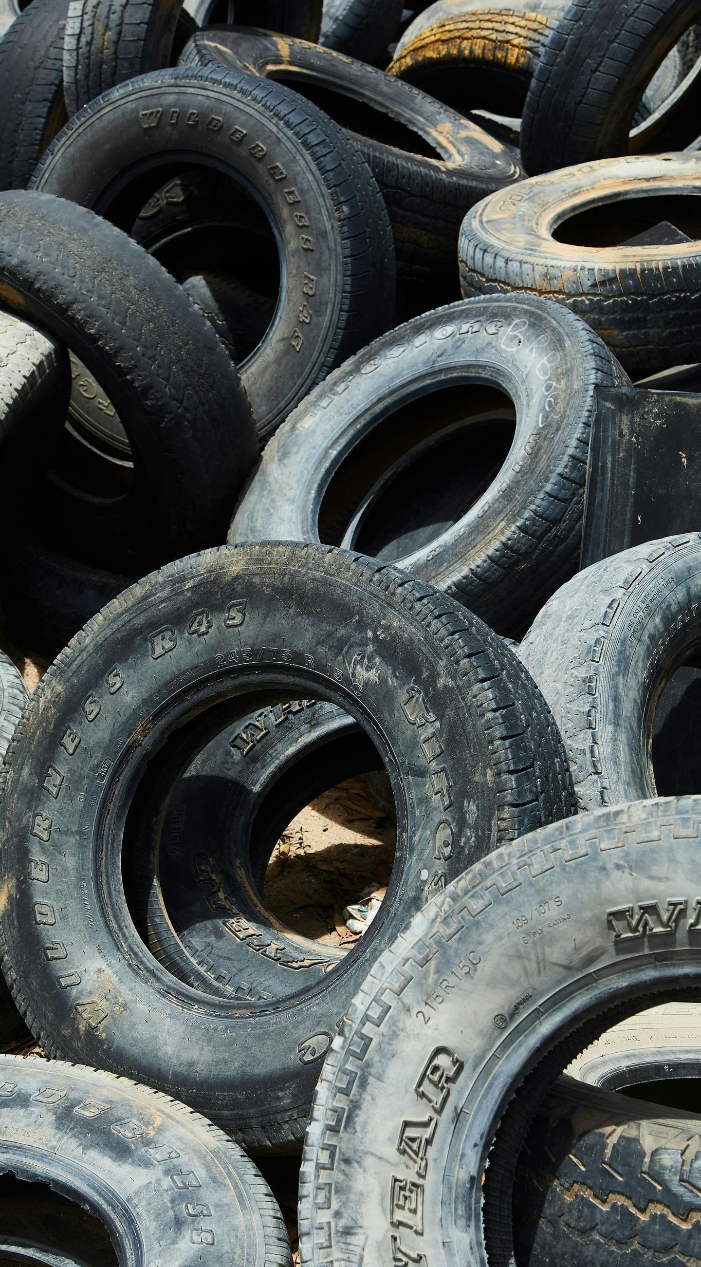 Pile of weathered, used tires; some with visible tread, outdoors.