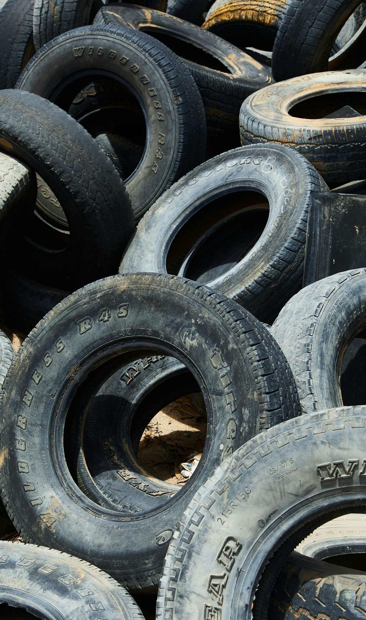 Pile of weathered, used tires; some with visible tread, outdoors.