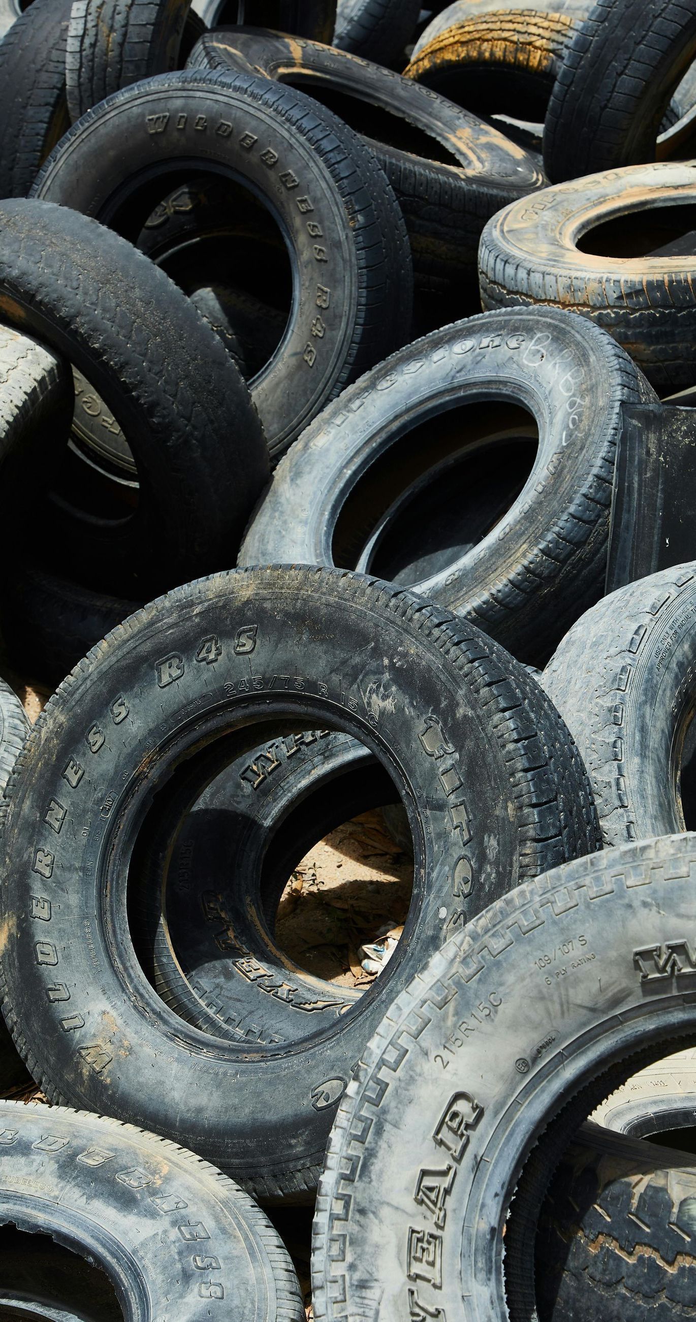 Pile of weathered, used tires; some with visible tread, outdoors.