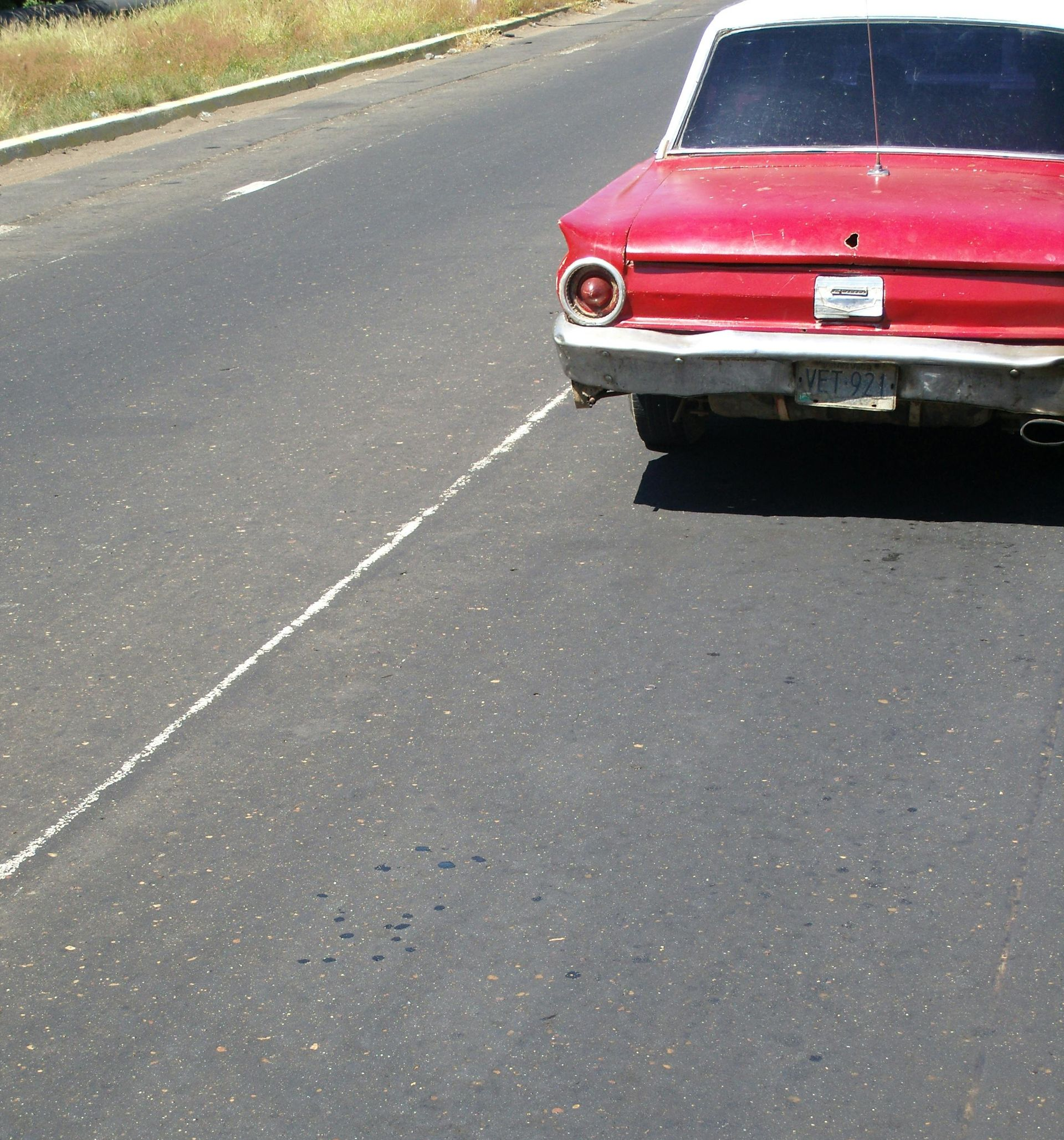 A red vintage car parked on the shoulder of an asphalt road.