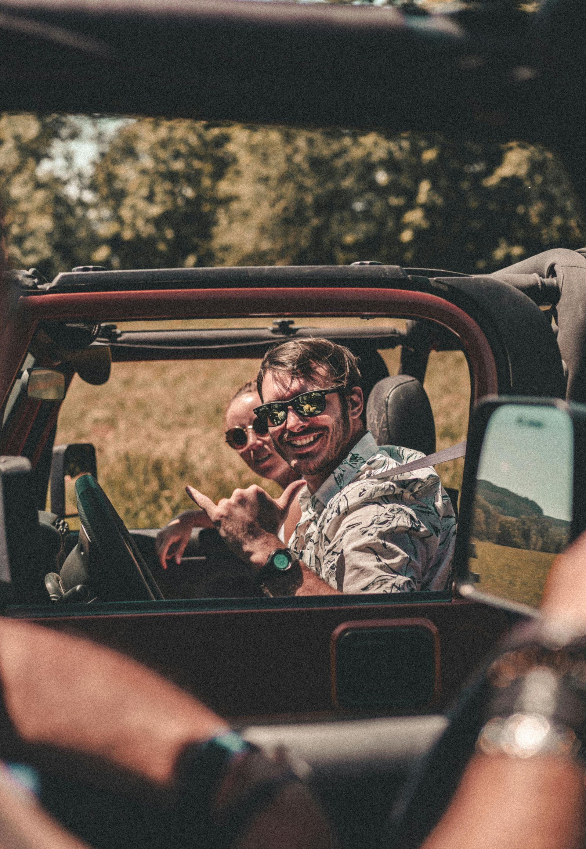 Two people smiling in a red open-top vehicle on a sunny road, with another passenger in the foreground