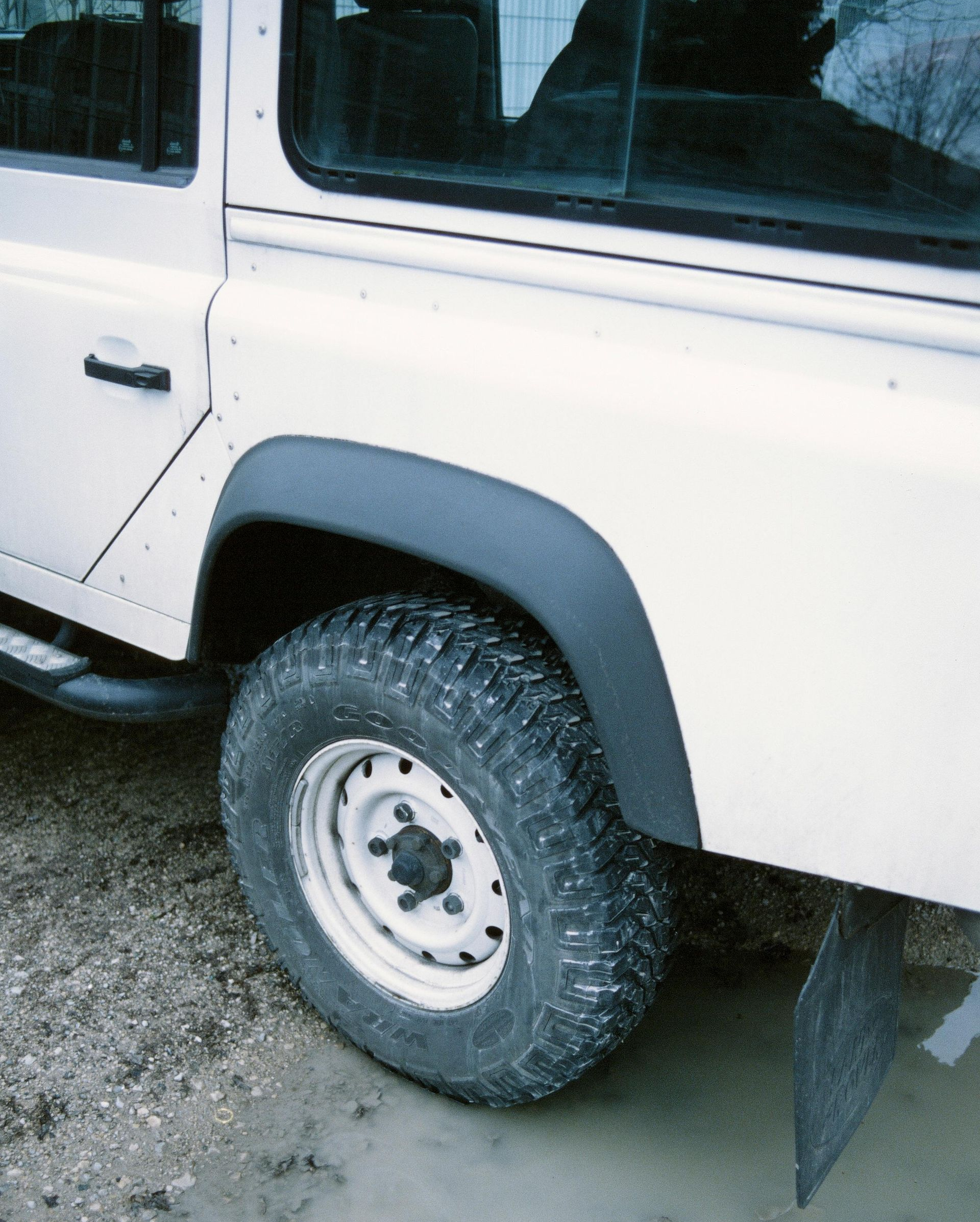 White off-road vehicle's rear wheel in muddy water, black fender flares.