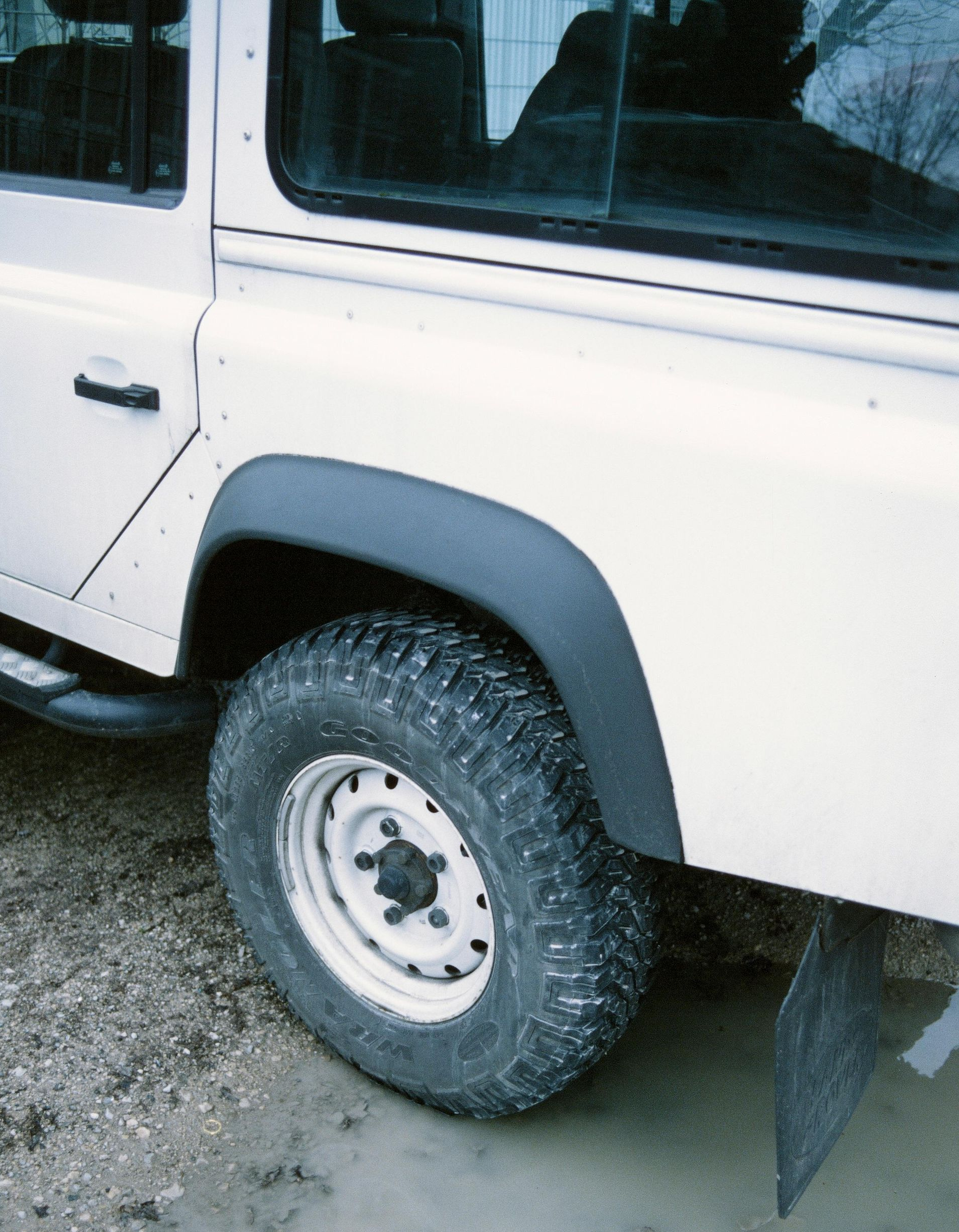White off-road vehicle's rear wheel in muddy water, black fender flares.