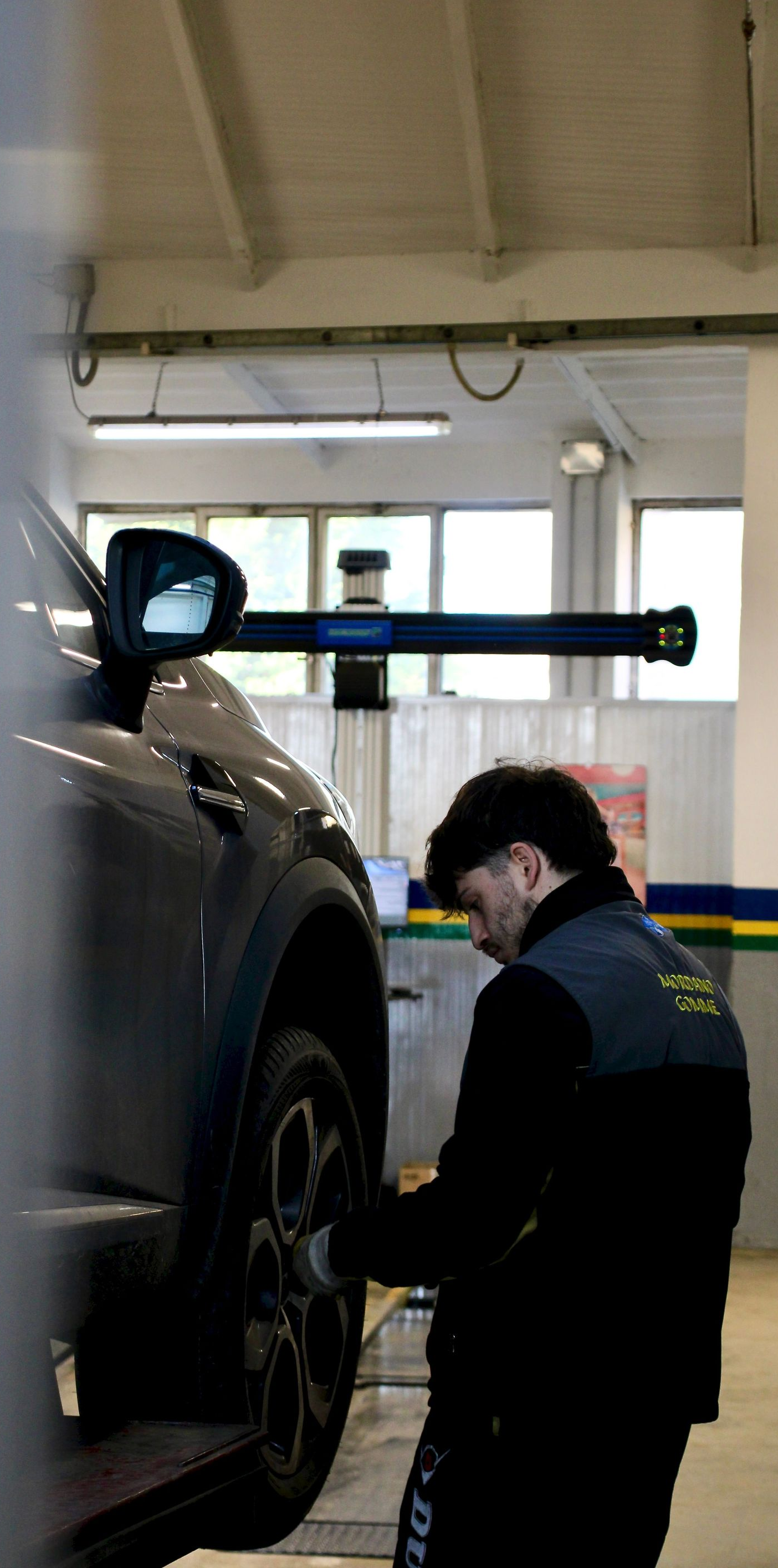 Mechanic in dark coveralls inspecting a raised car in an auto shop garage