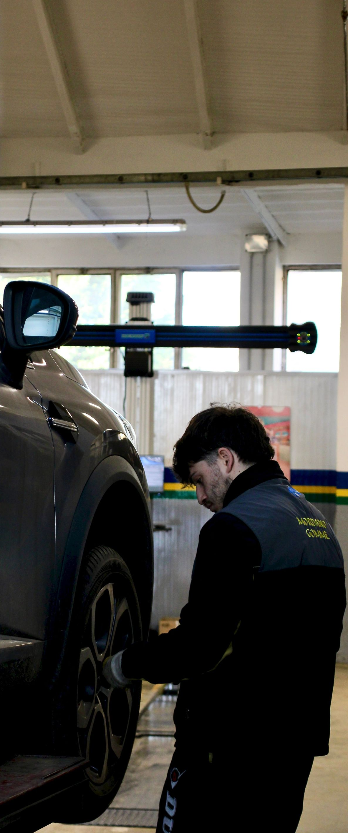 Mechanic in dark uniform inspecting a car wheel in a garage lift bay