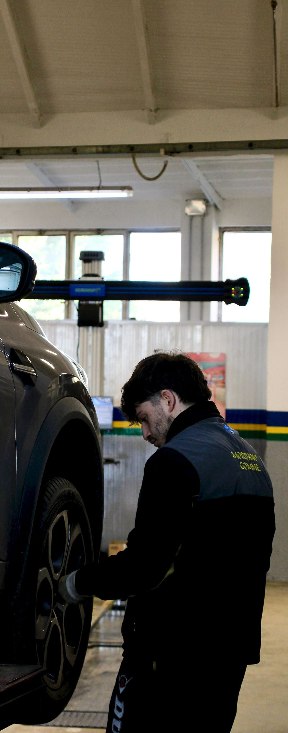 Mechanic in dark coveralls inspecting a raised car in an auto shop garage