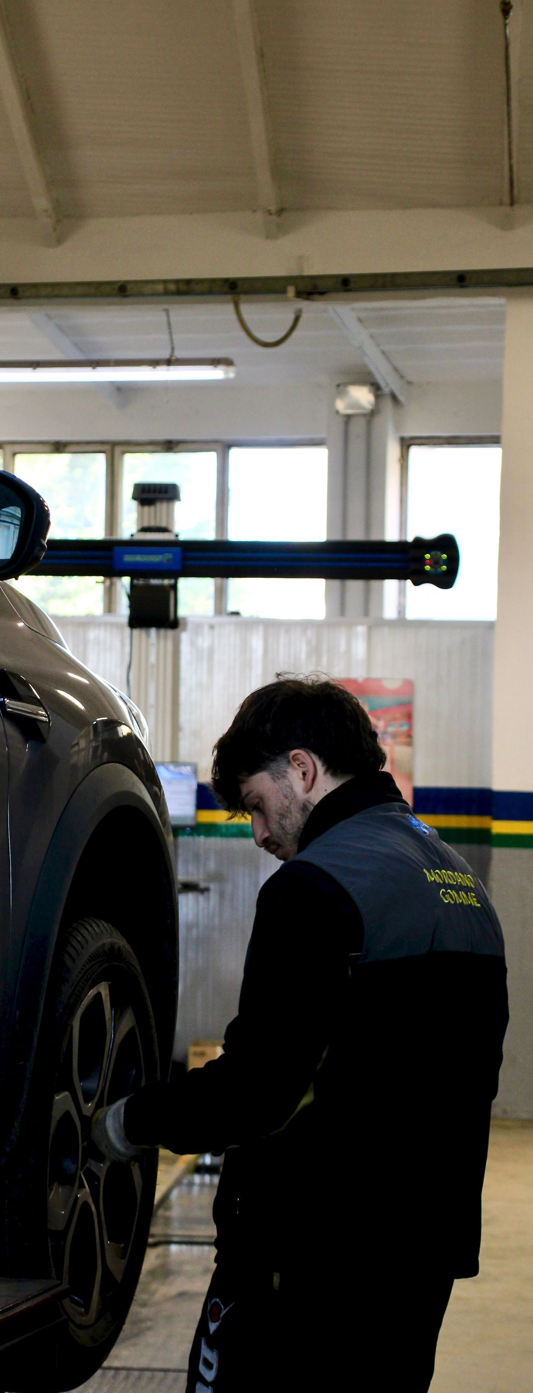 Mechanic in dark coveralls inspecting a raised car in an auto shop garage