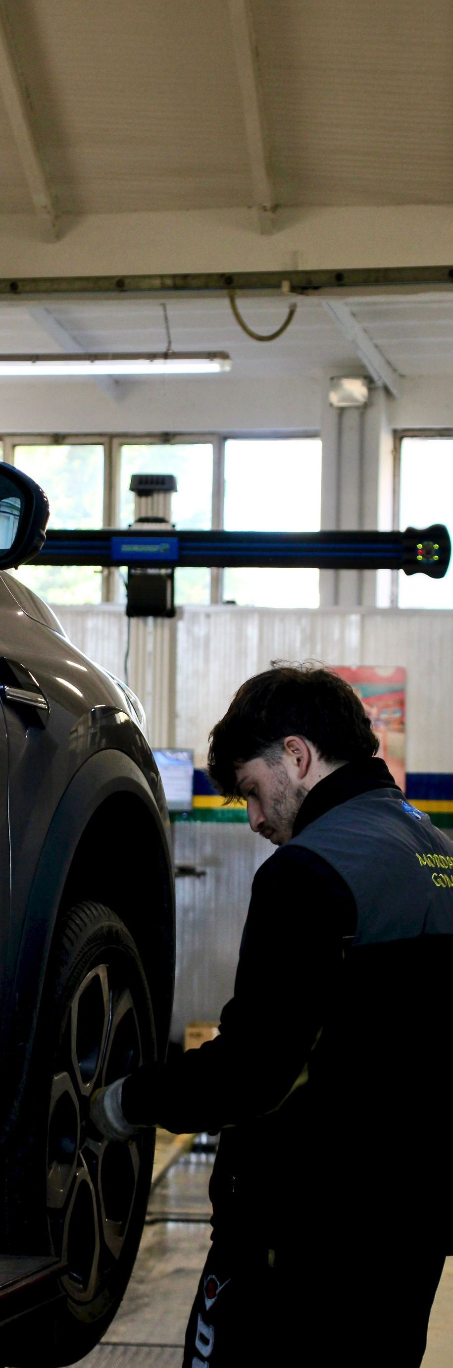 Mechanic in dark uniform inspecting a car wheel in a garage lift bay