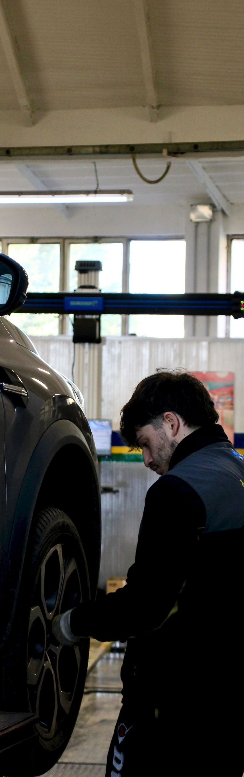 Mechanic in dark uniform inspecting a car wheel in a garage lift bay