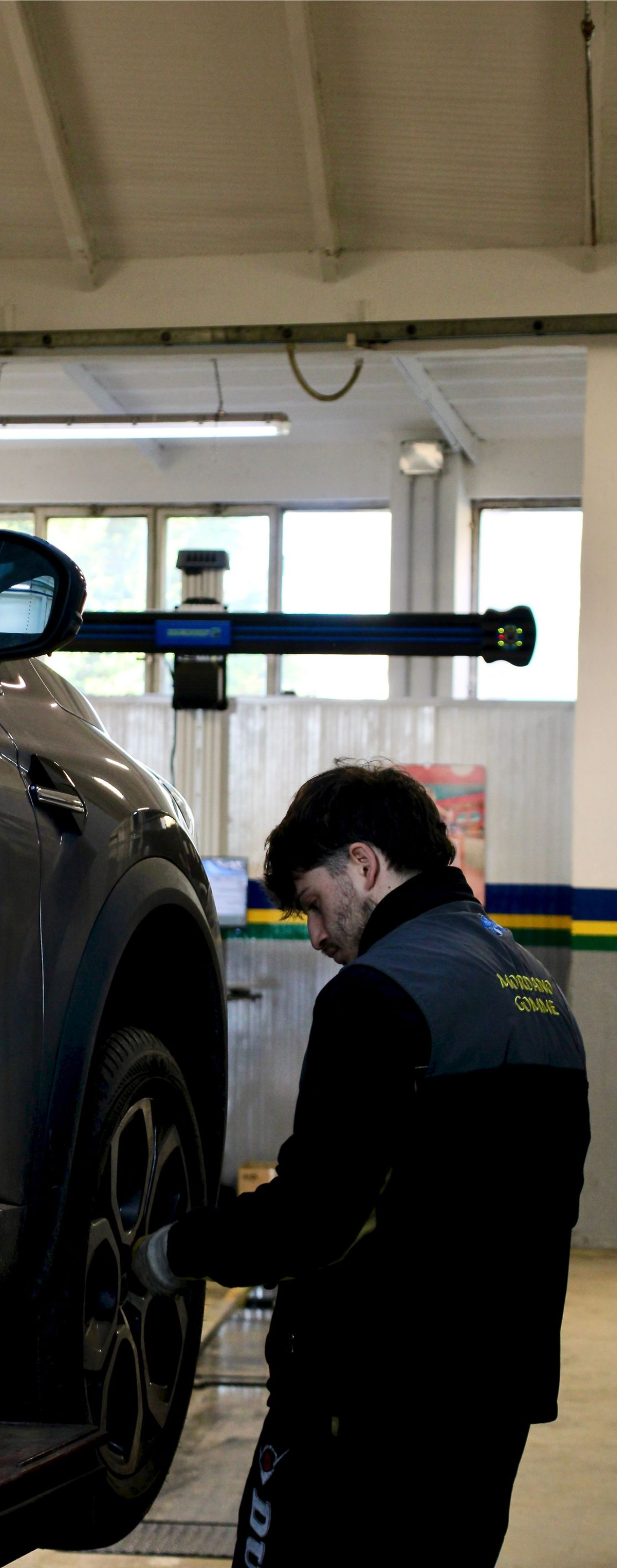 Mechanic in dark coveralls inspecting a raised car in an auto shop garage