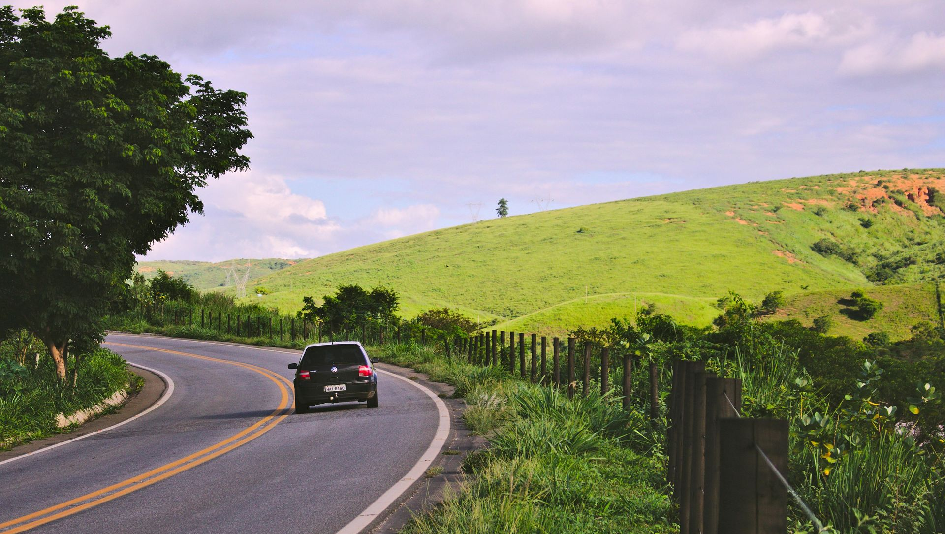 Car driving on a winding road through a green, hilly landscape.