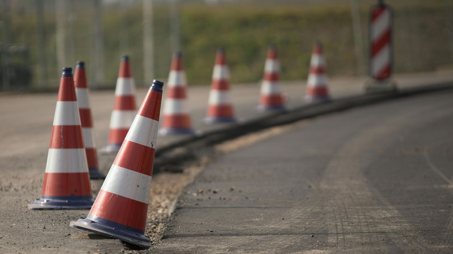 Red-and-white traffic cones lining a curved roadside edge beside a blurred roadway.