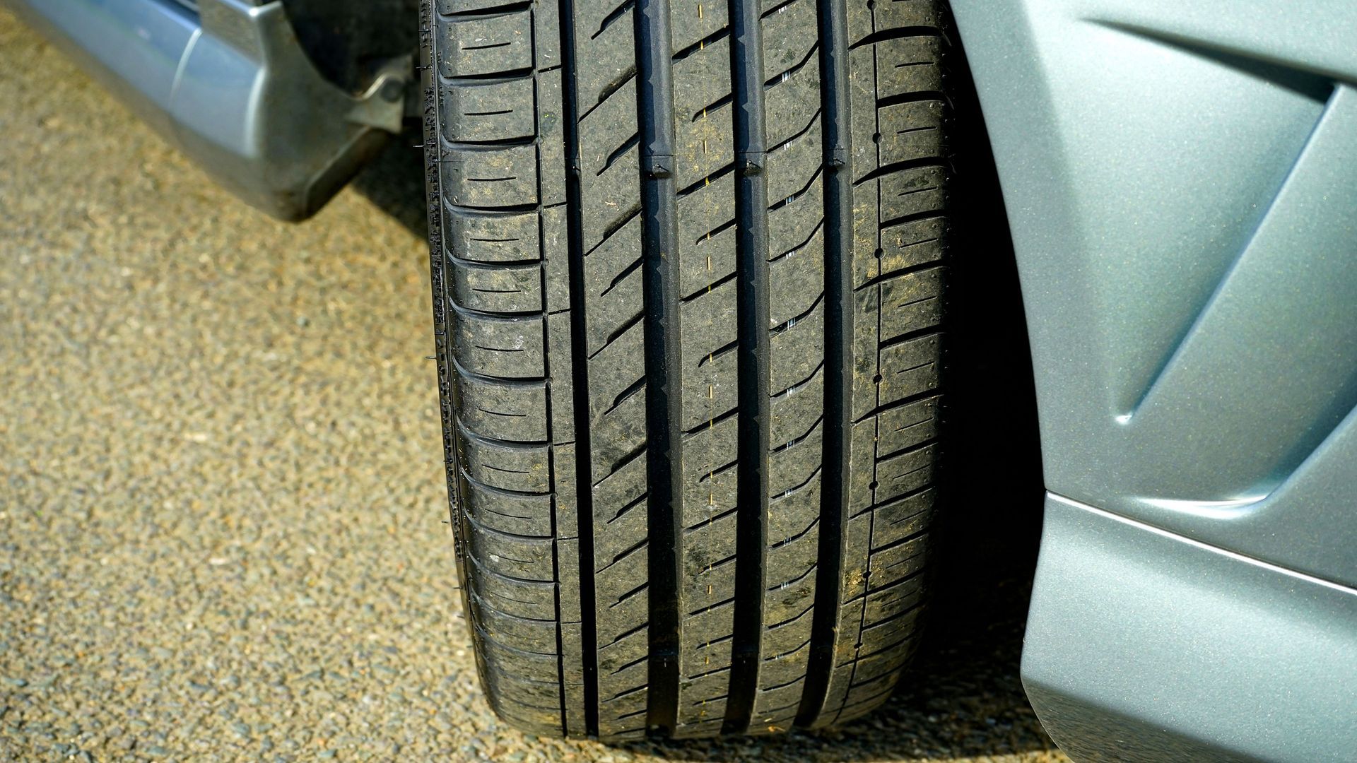 Close-up of a car tire beside a silver vehicle on a paved road.