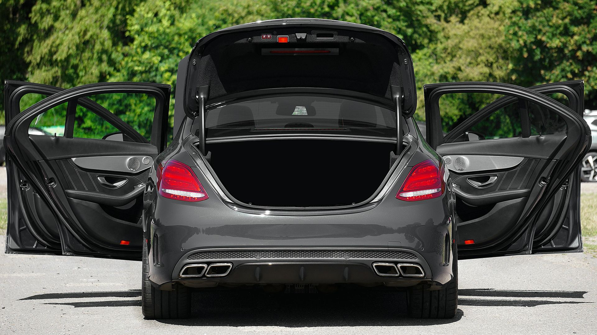 Black sports car with all doors and trunk open, parked on a road with trees in the background