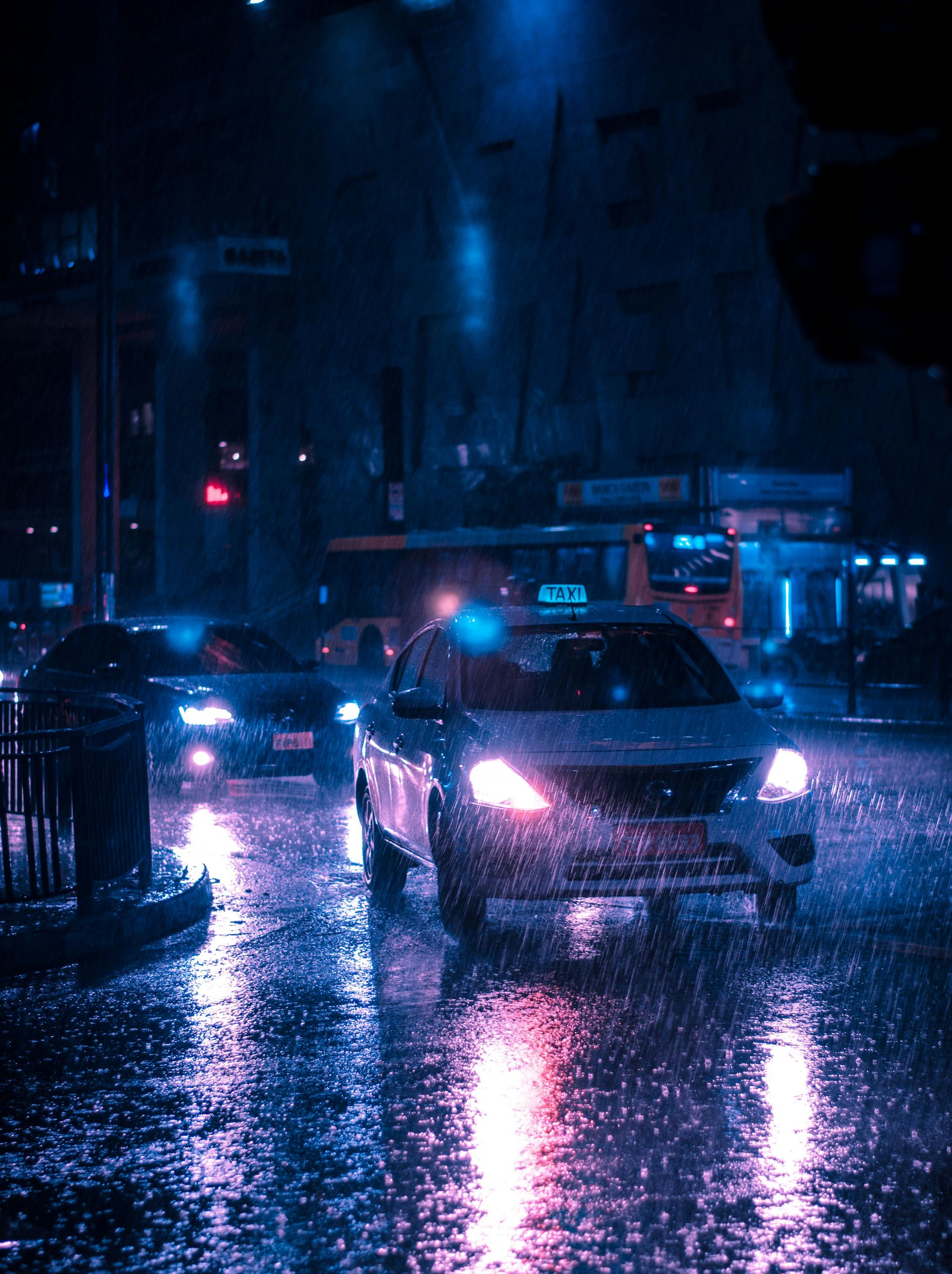 Cars driving on a wet city street at night. Rain reflects the blue and pink streetlights.