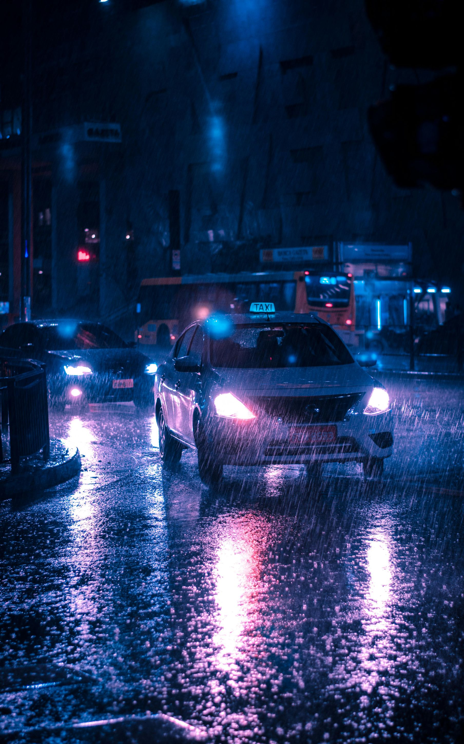 Cars driving on a wet city street at night. Rain reflects the blue and pink streetlights.