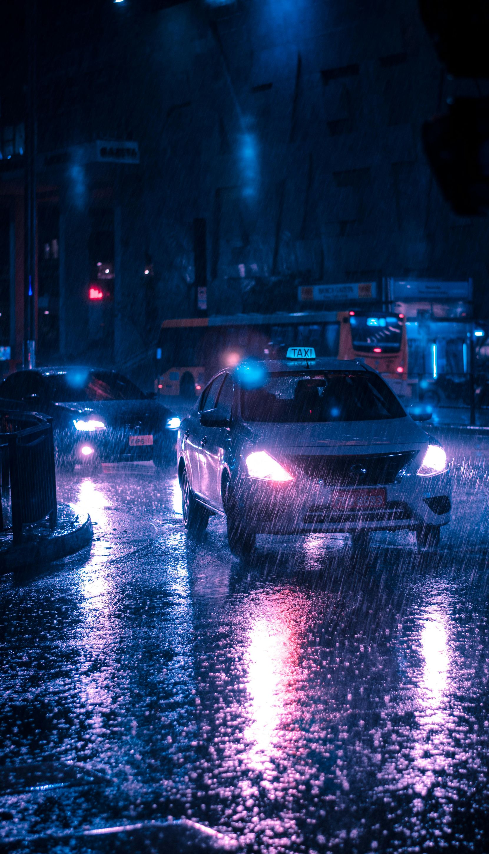Cars driving on a wet city street at night. Rain reflects the blue and pink streetlights.