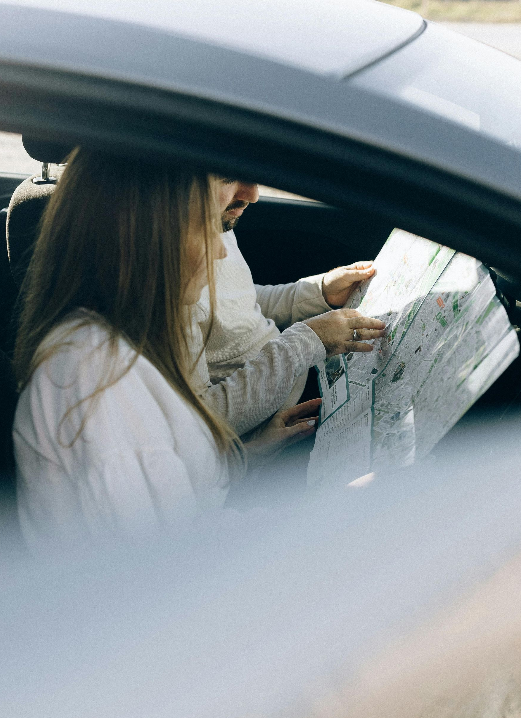 Person inside a car looking at a map while another person points to a location.