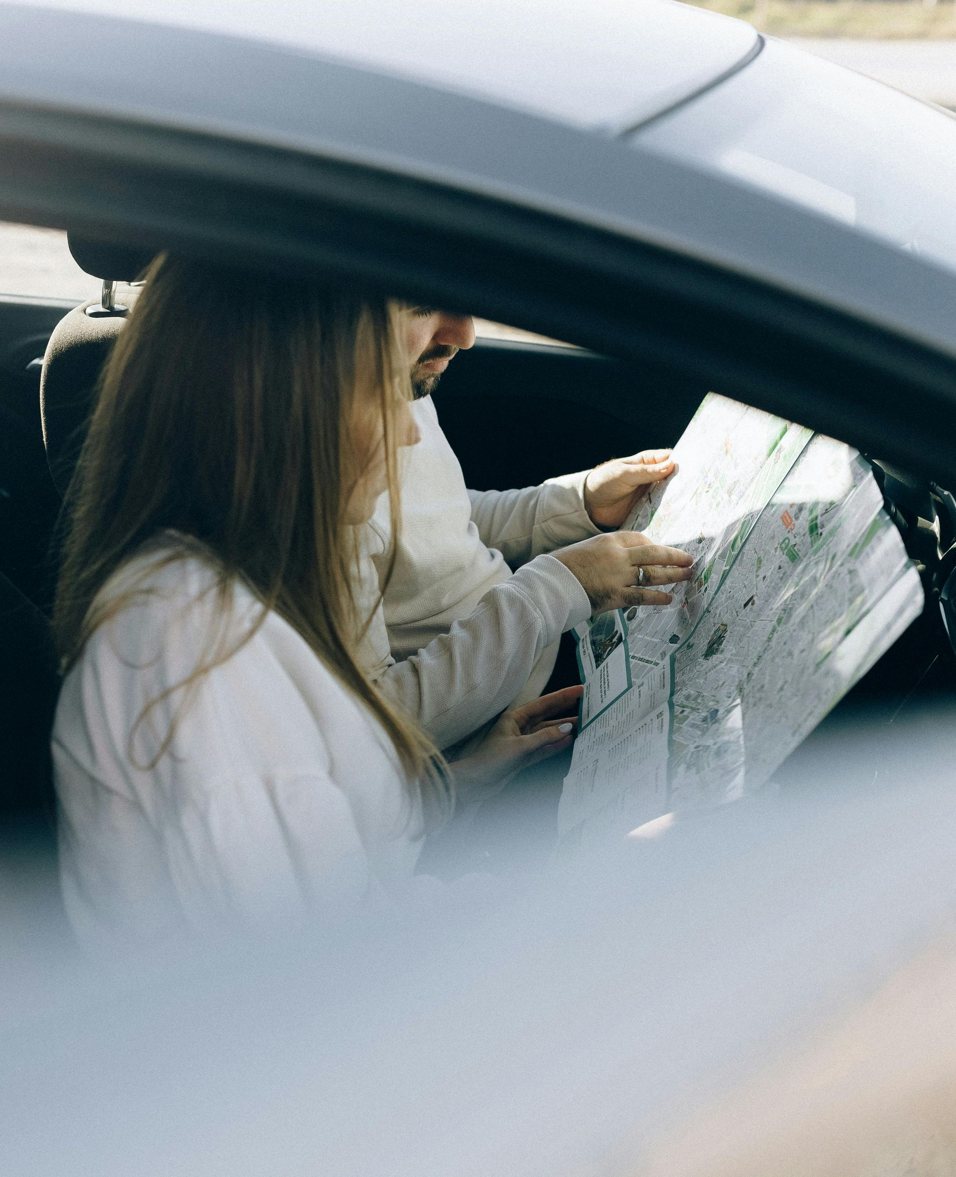 Person inside a car looking at a map while another person points to a location.