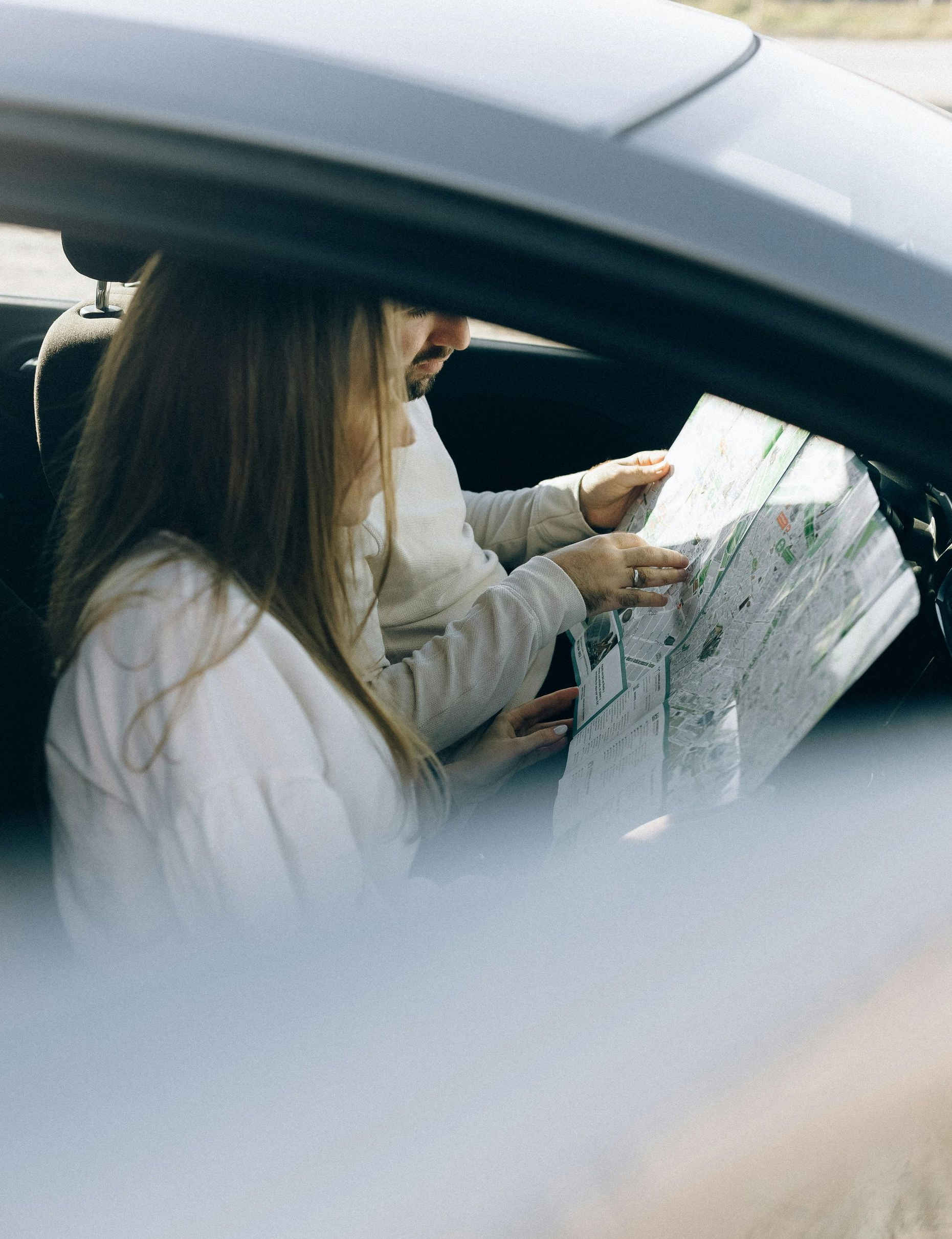 Person inside a car looking at a map while another person points to a location.