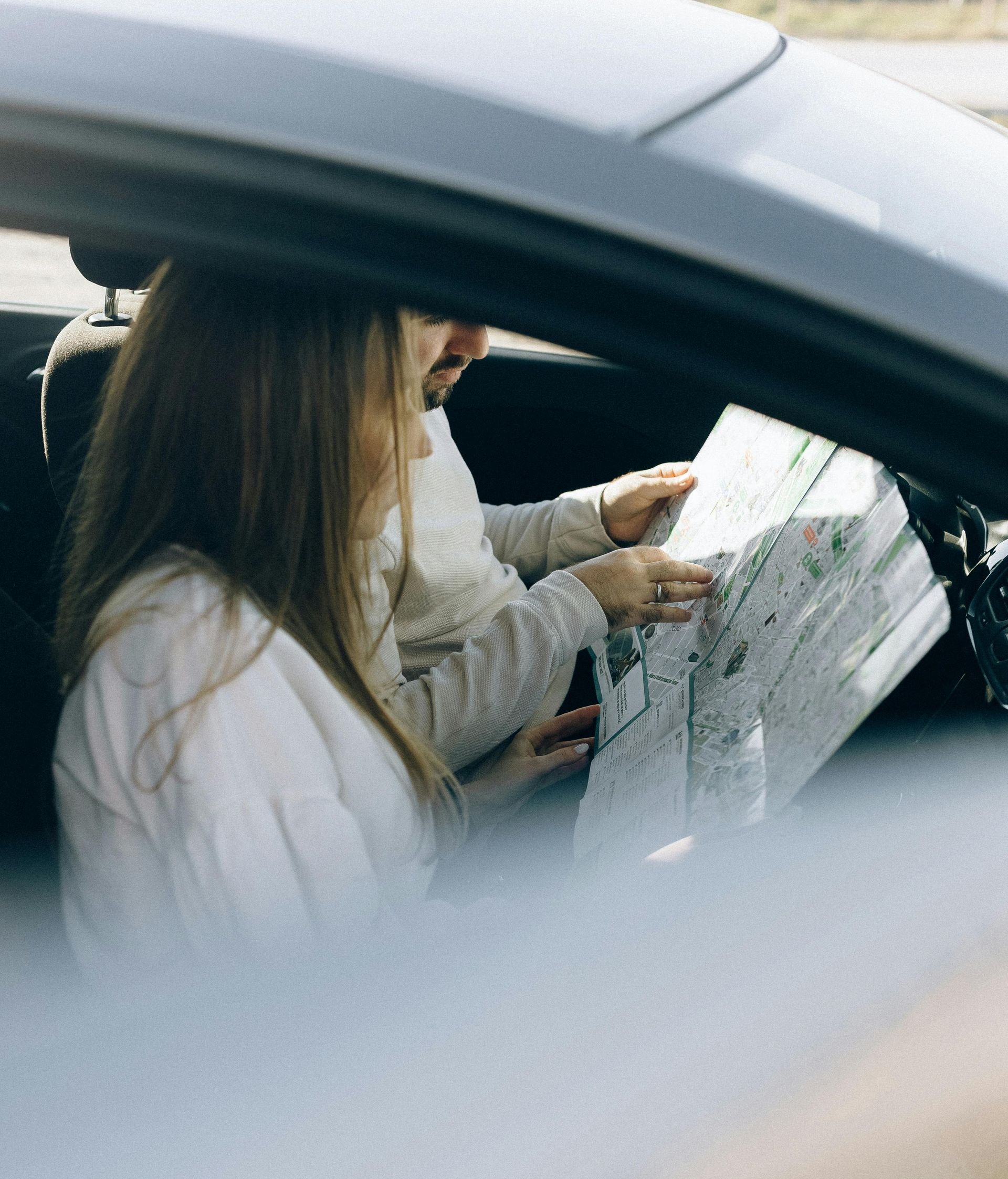 Person inside a car looking at a map while another person points to a location.