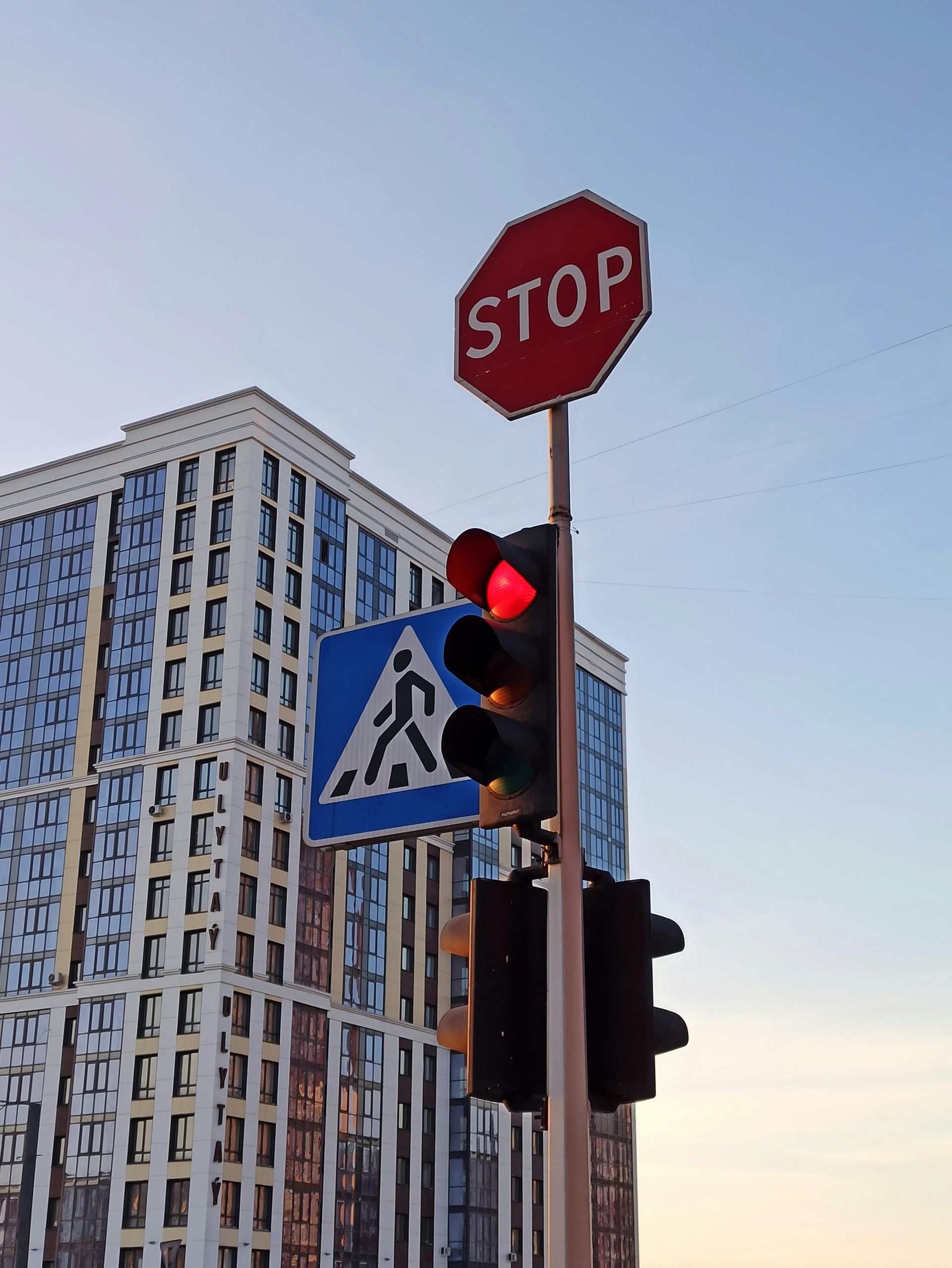Stop sign and red traffic light beside a crosswalk sign, with a tall building in the background.