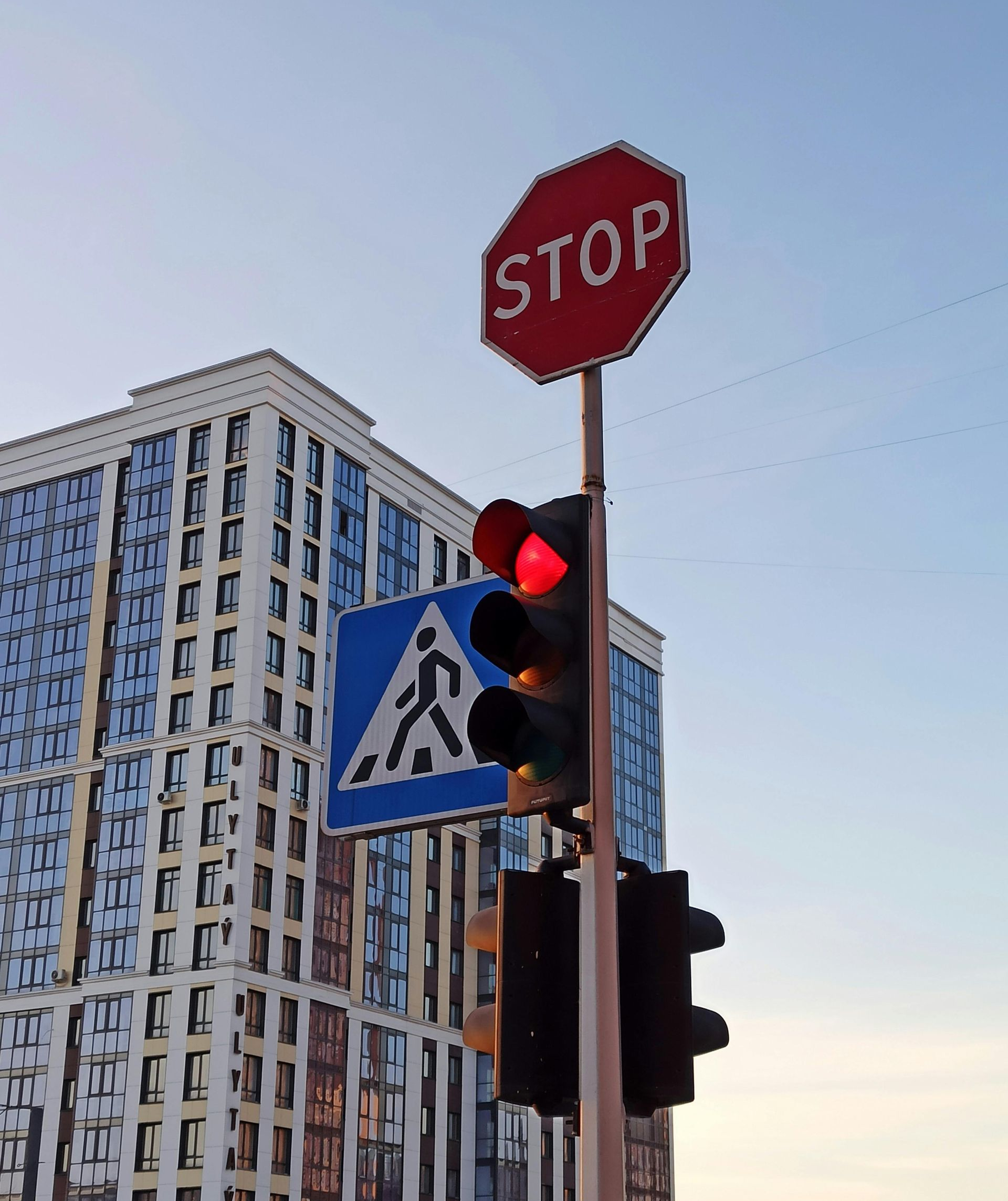 Stop sign and red traffic light beside a crosswalk sign, with a tall building in the background.