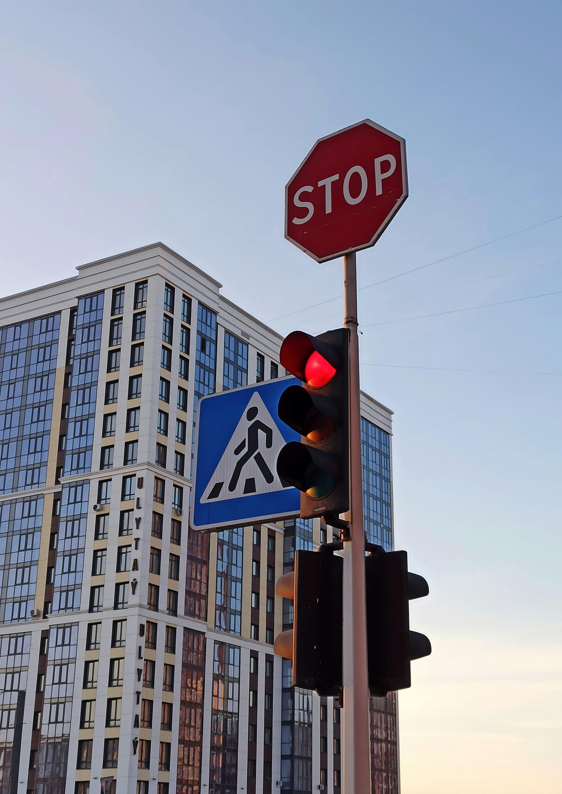 Stop sign and red traffic light beside a crosswalk sign, with a tall building in the background.