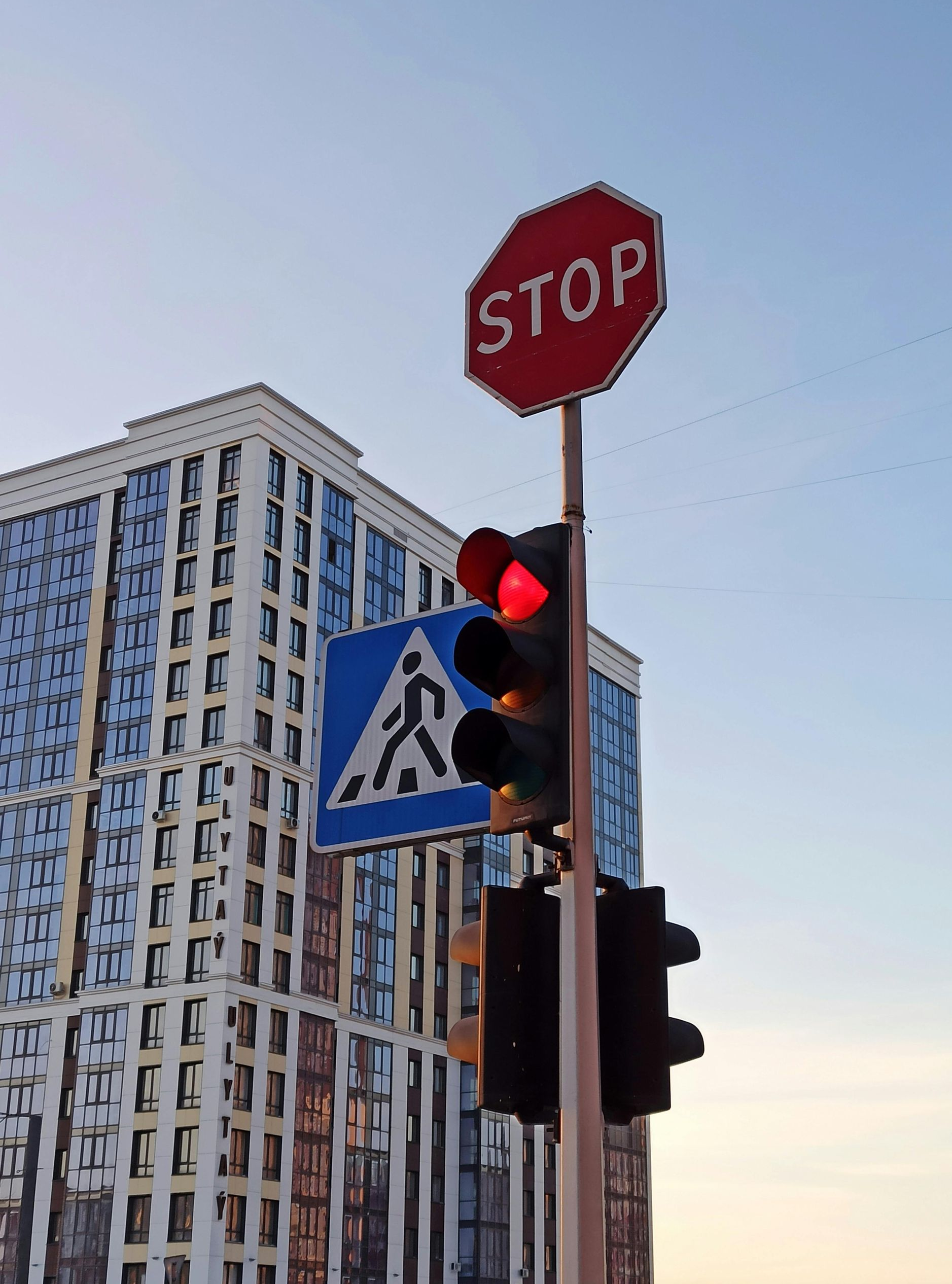 Stop sign and red traffic light beside a crosswalk sign, with a tall building in the background.
