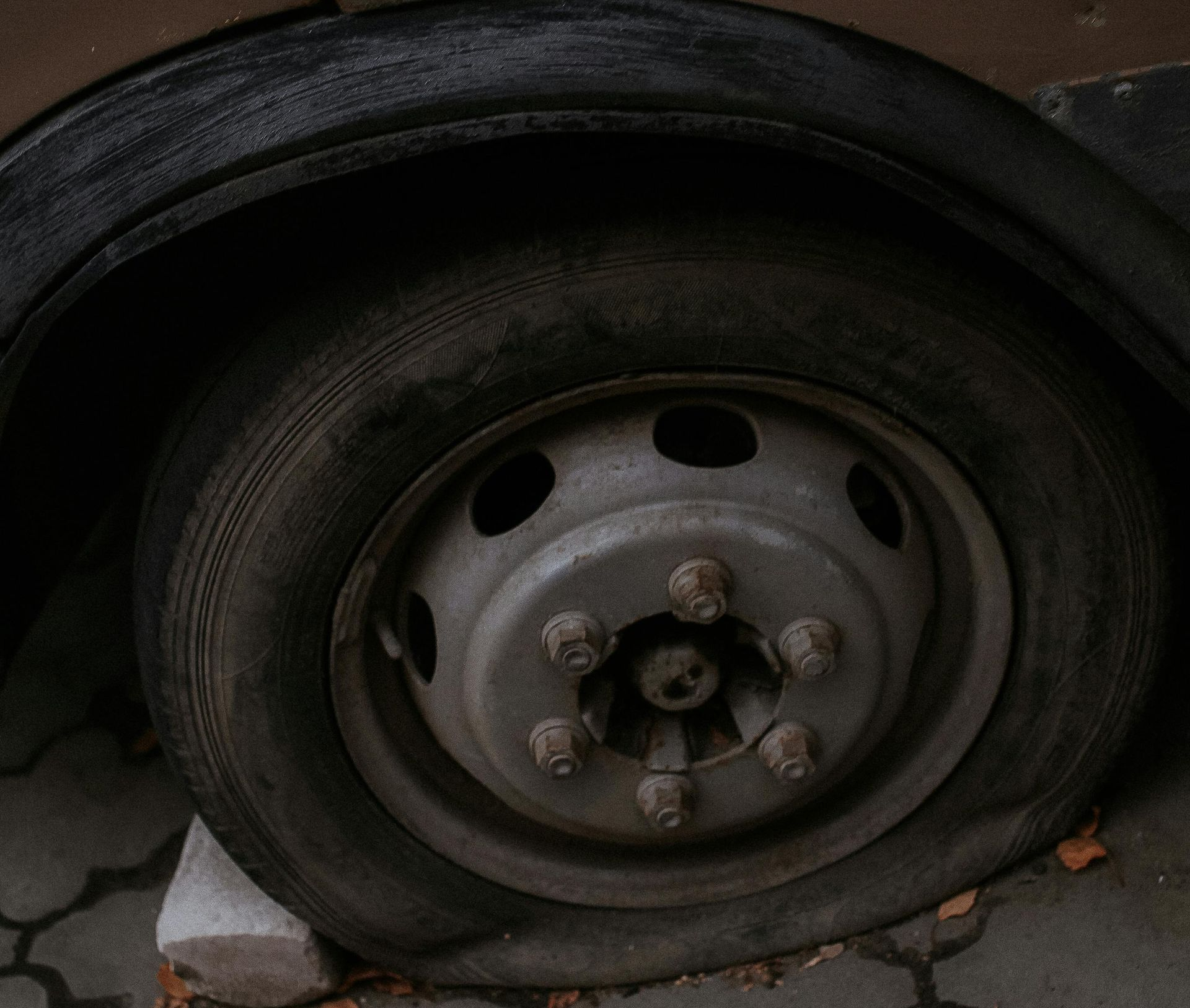 Flat tire on a vehicle's wheel, resting on a concrete block, in an outdoor setting.