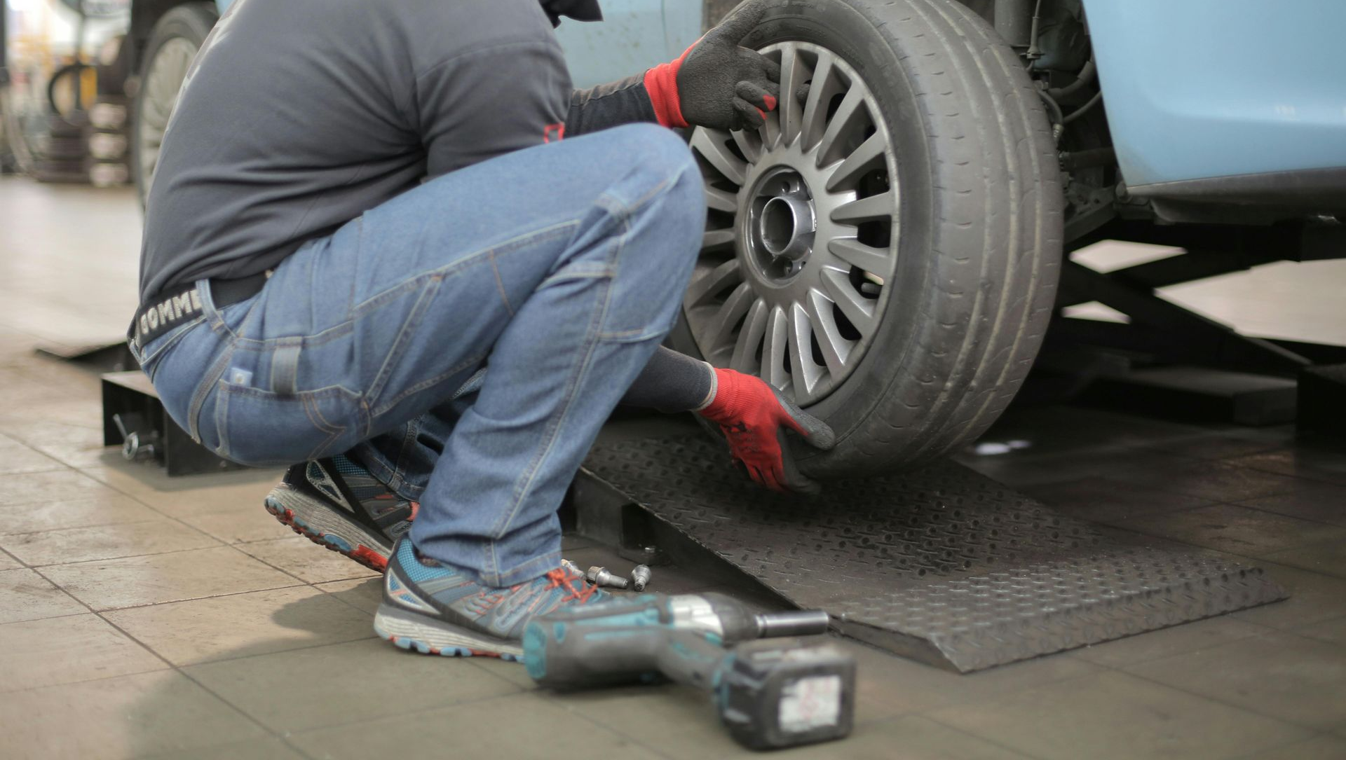 Mechanic changing a tire on a blue car in a garage.