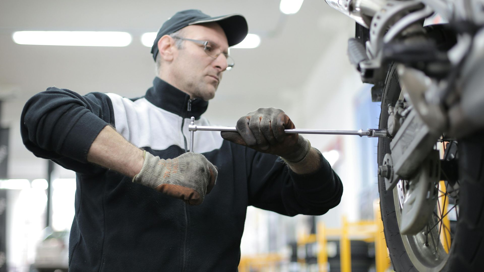 Mechanic in a workshop using a wrench to work on a motorcycle tire.