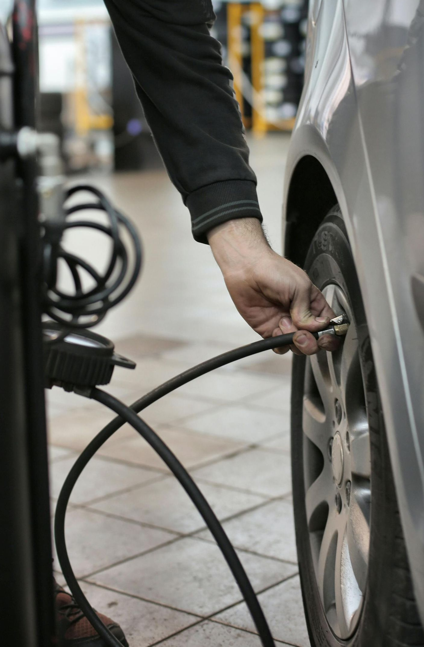 Person inflating a car tire with an air compressor in a garage.