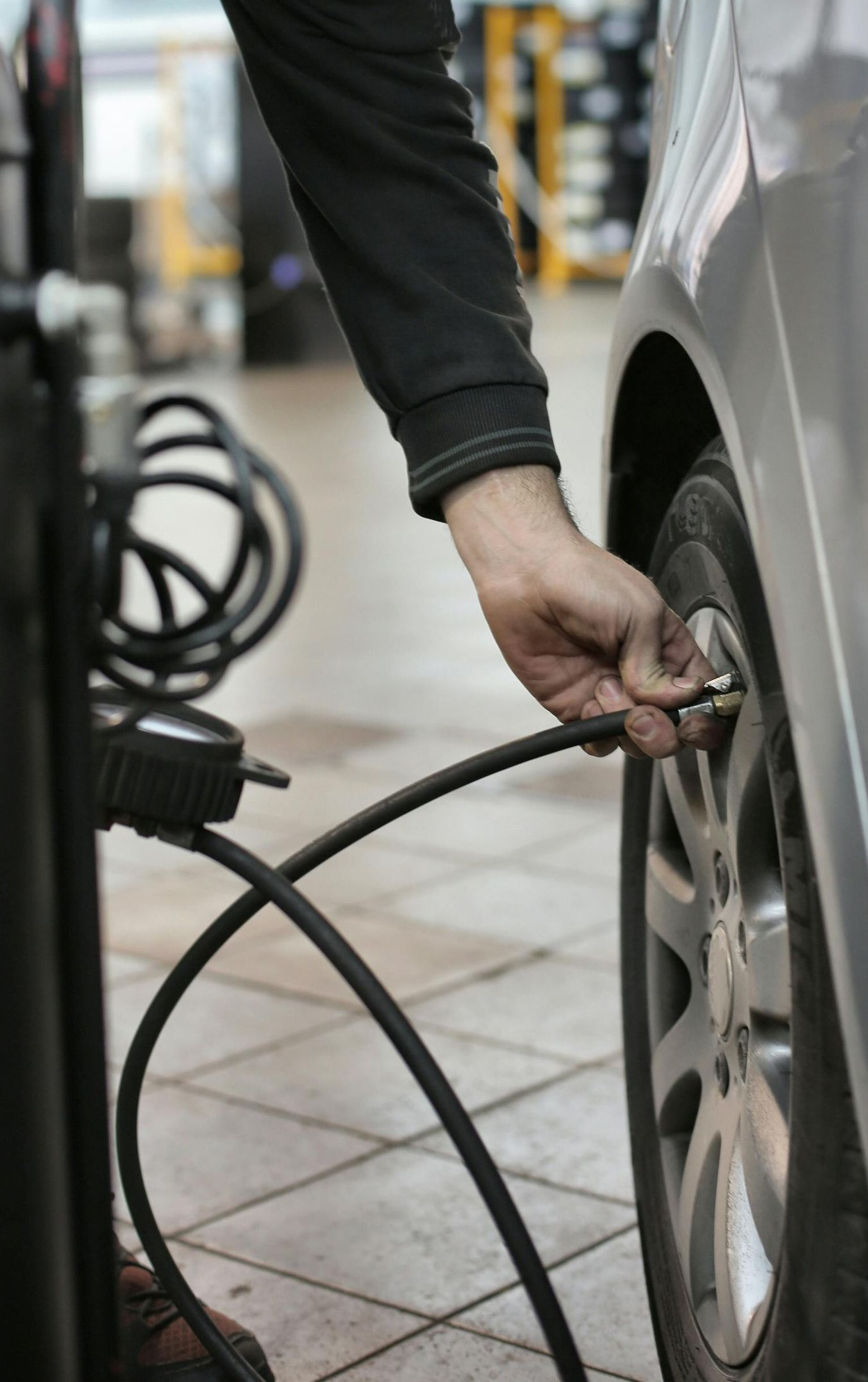 Person inflating a car tire with an air compressor in a garage.