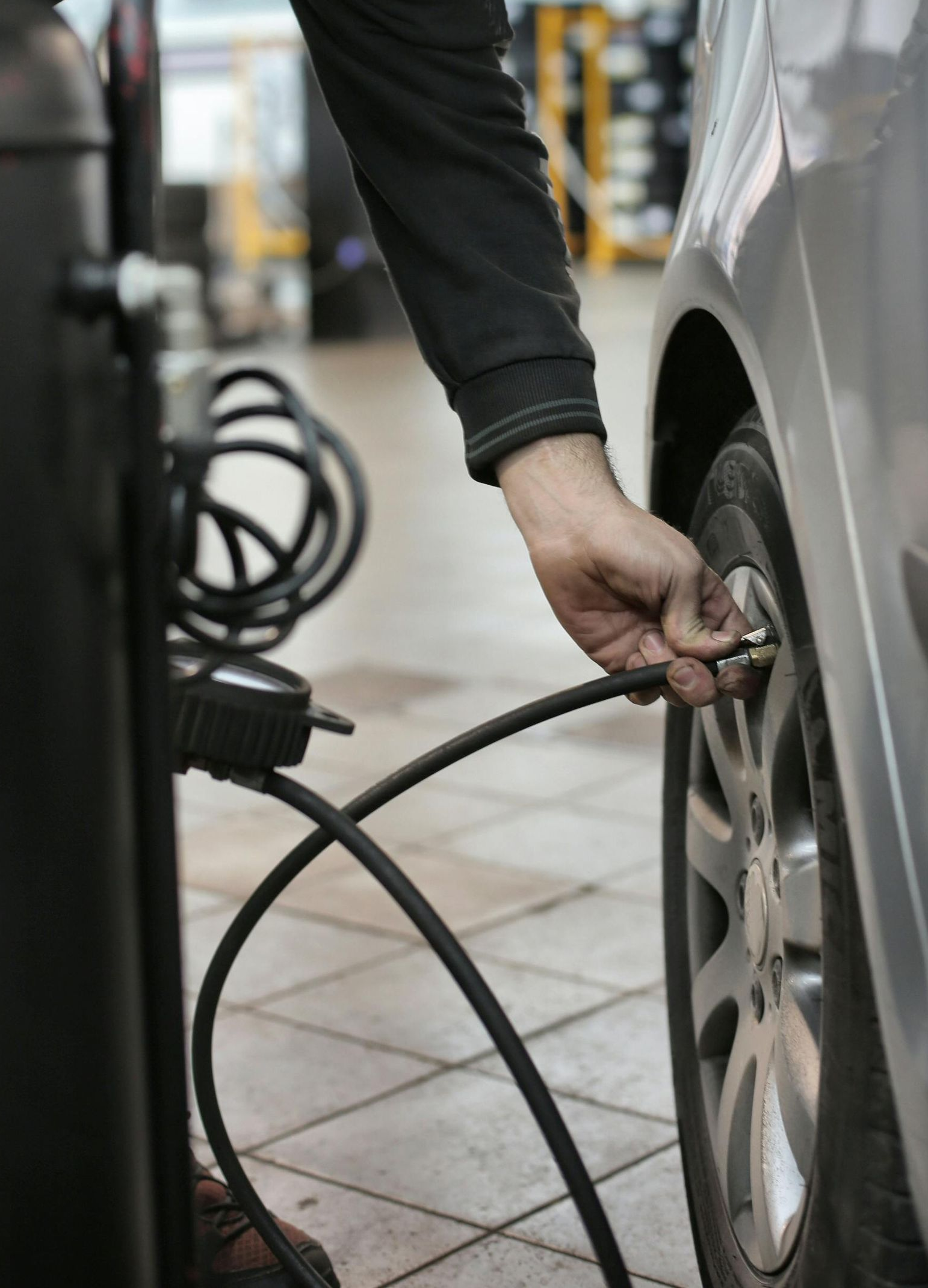 Person inflating a car tire with an air compressor in a garage.