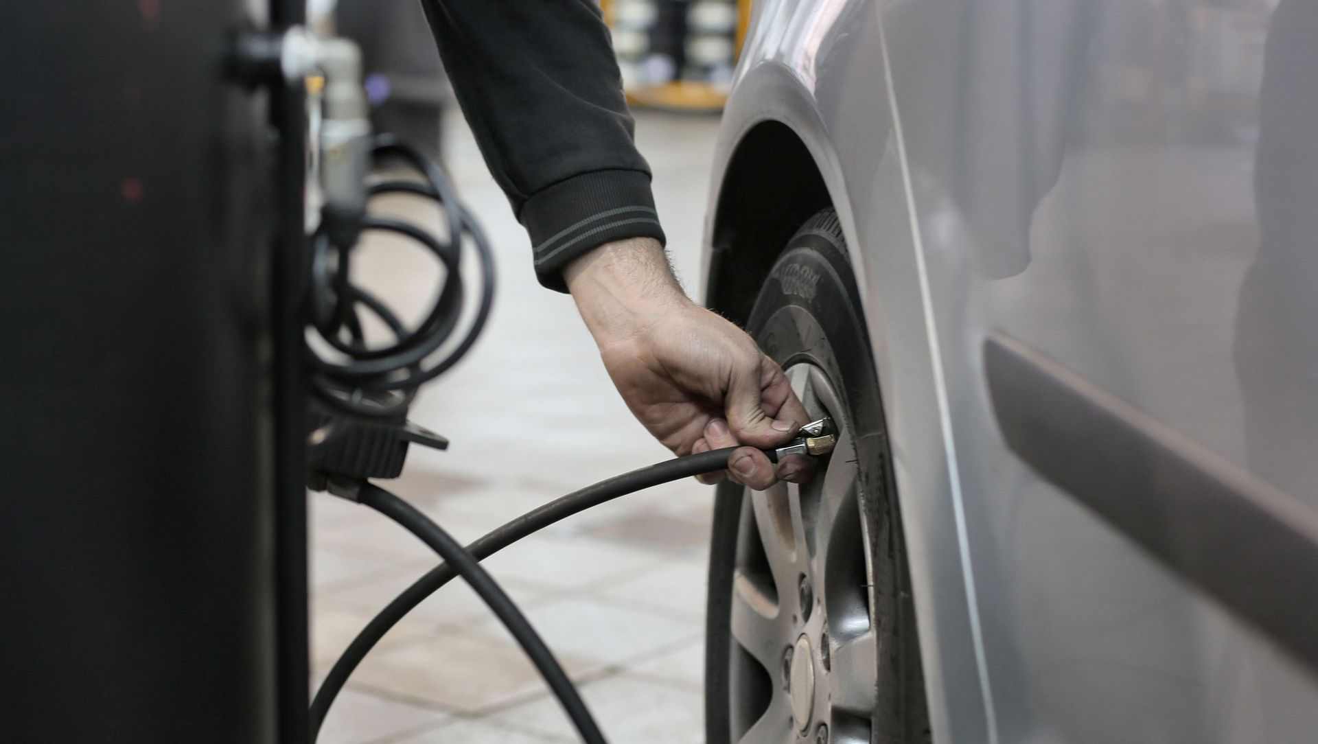 Person inflating a car tire with a pump at a service station