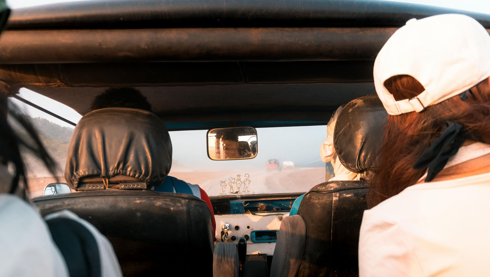 People inside a car driving at sunset, viewed from the back seat.
