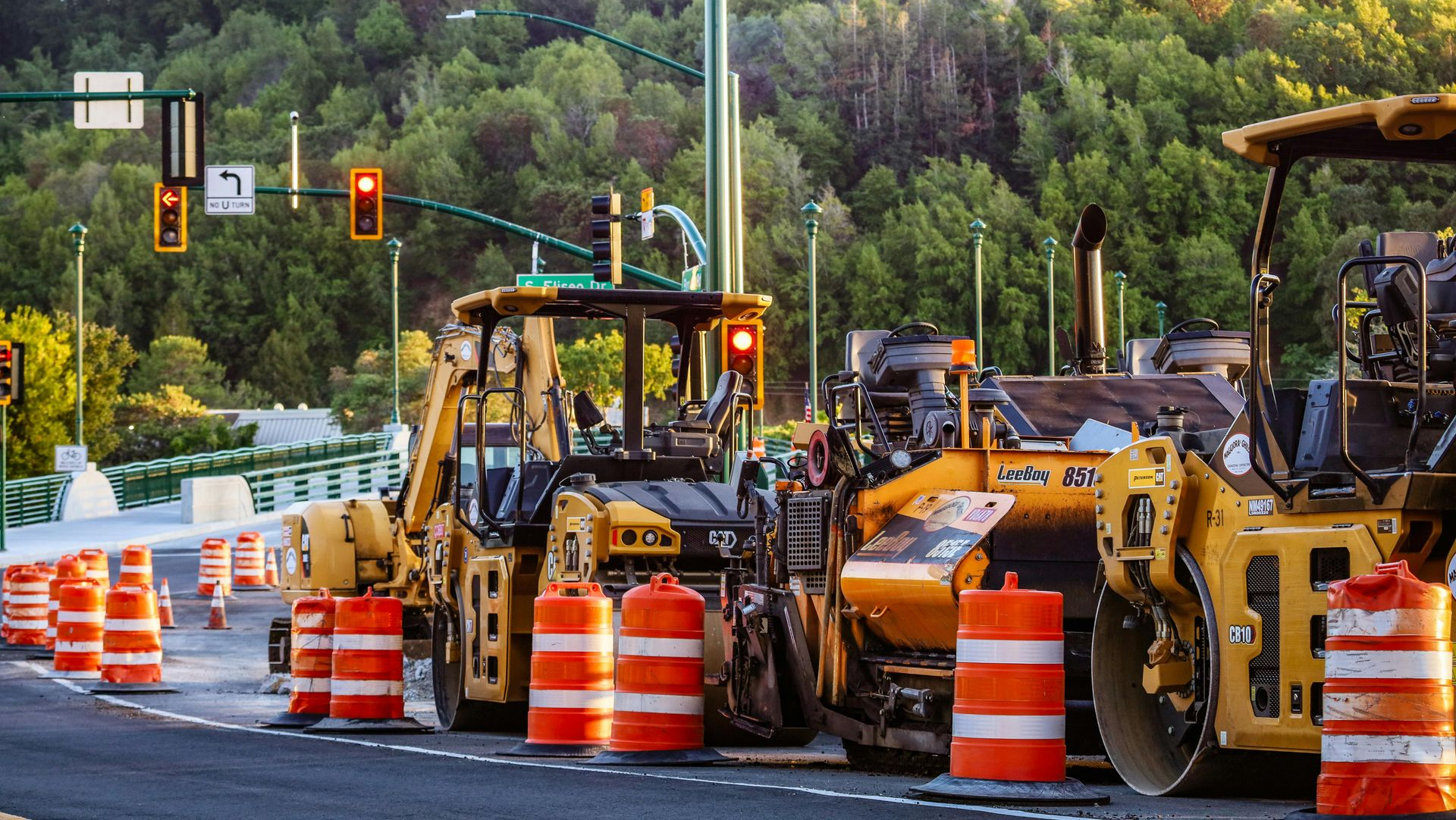 Road construction with yellow heavy equipment, orange barrels, and traffic lights at an intersection