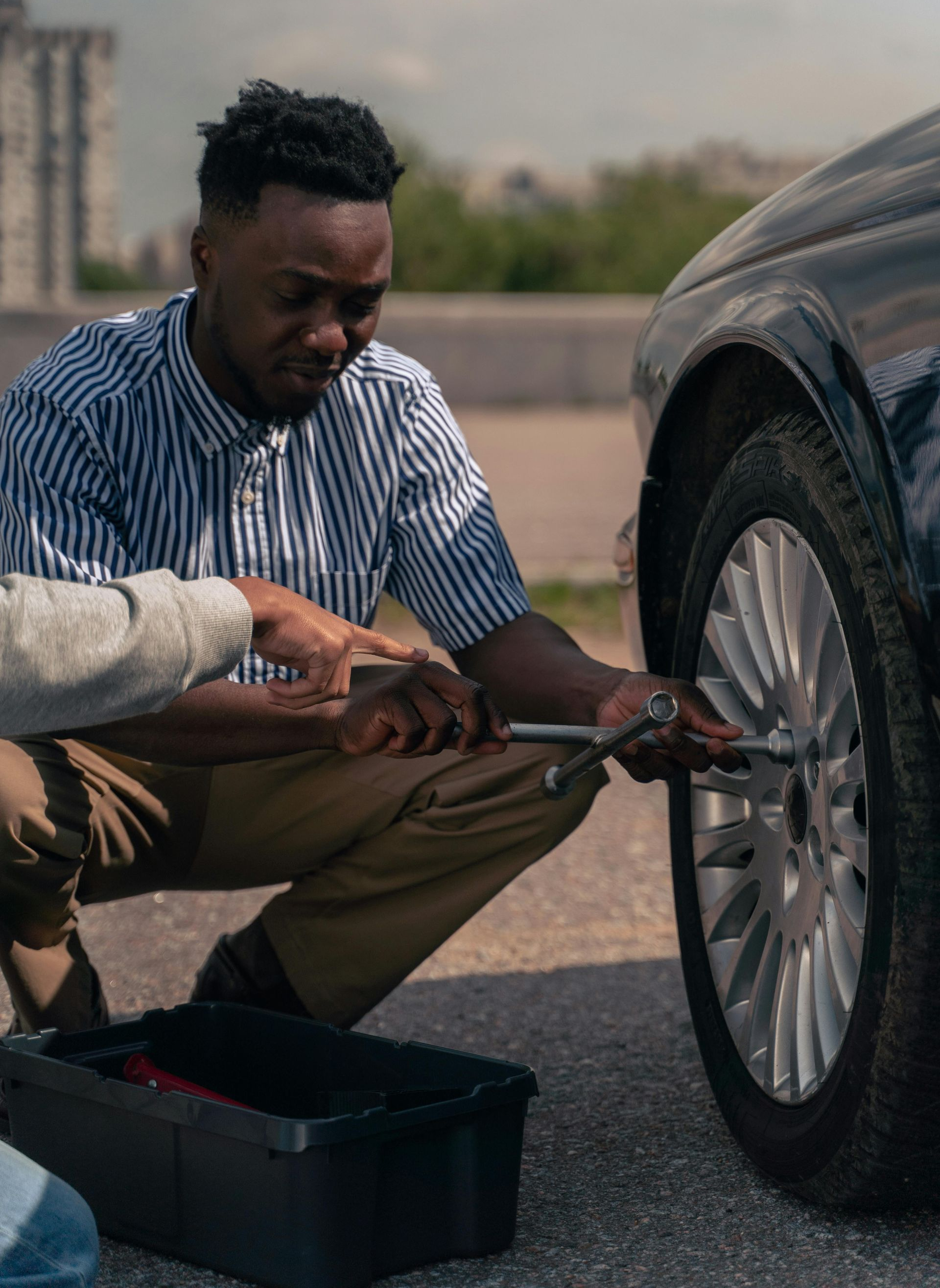Man crouches next to a car, using a wrench. A toolbox is on the ground.