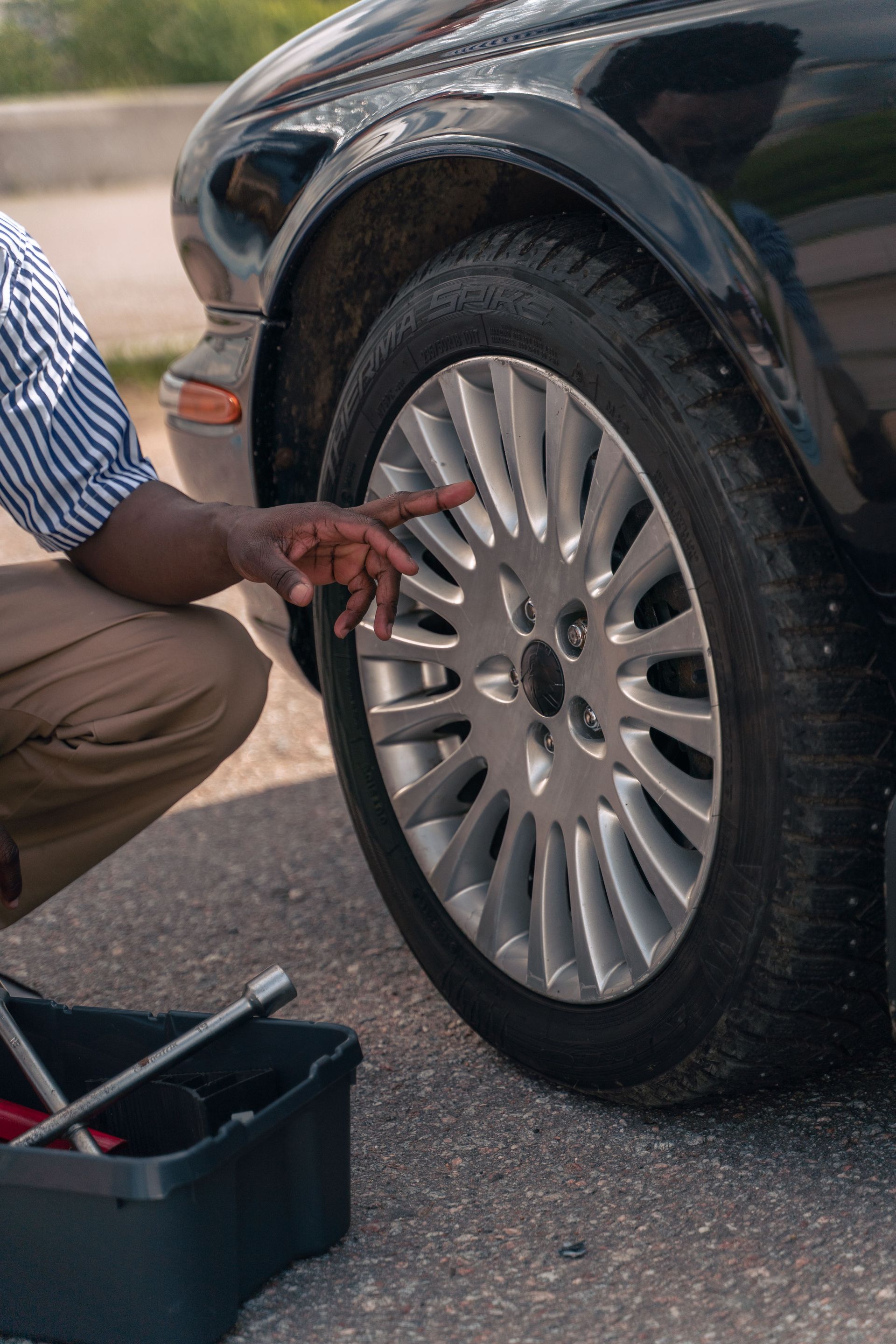 Mechanic checking a car tire beside an open toolbox on pavement