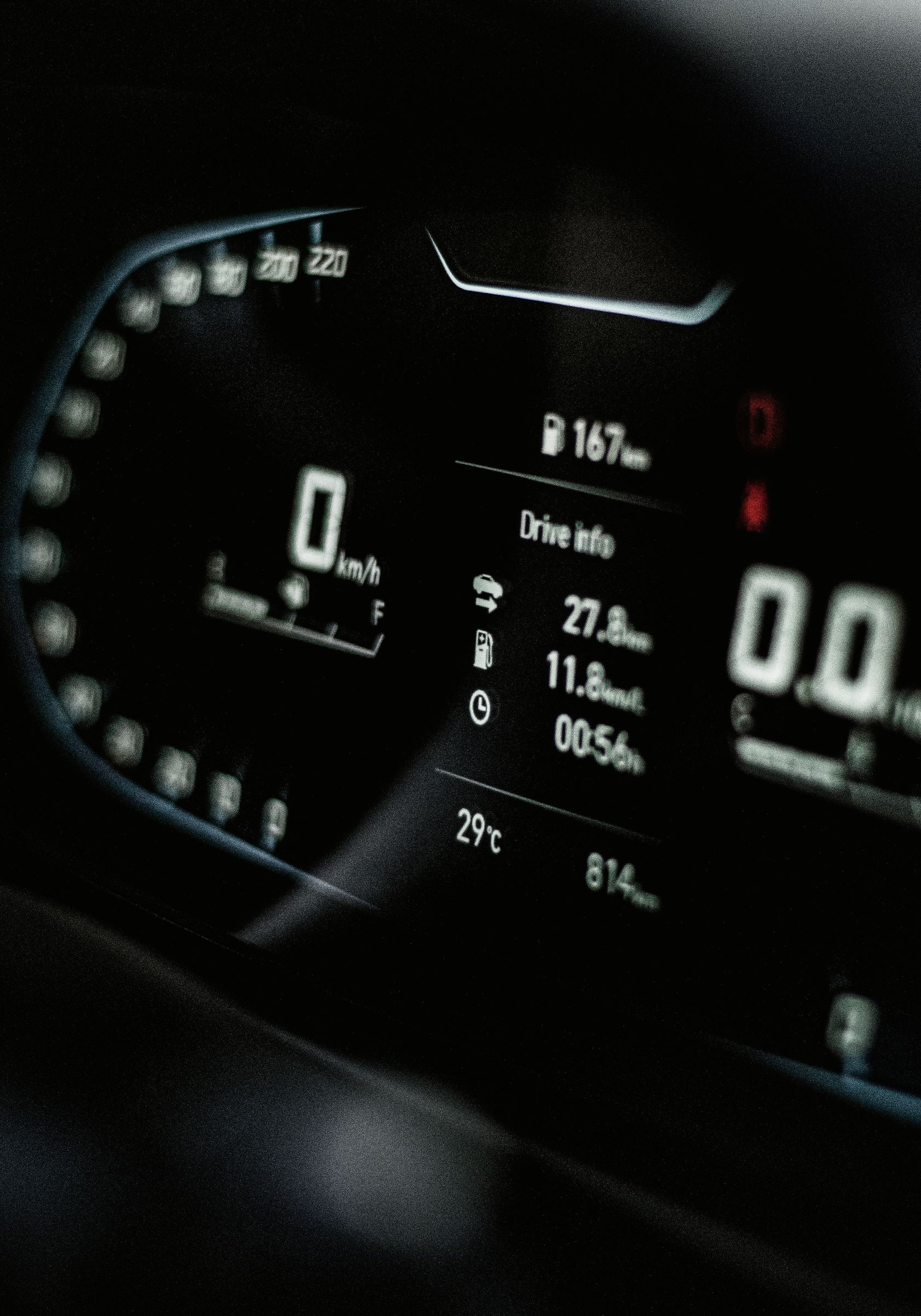 Car dashboard digital instrument cluster showing speed, fuel, and driving range at night