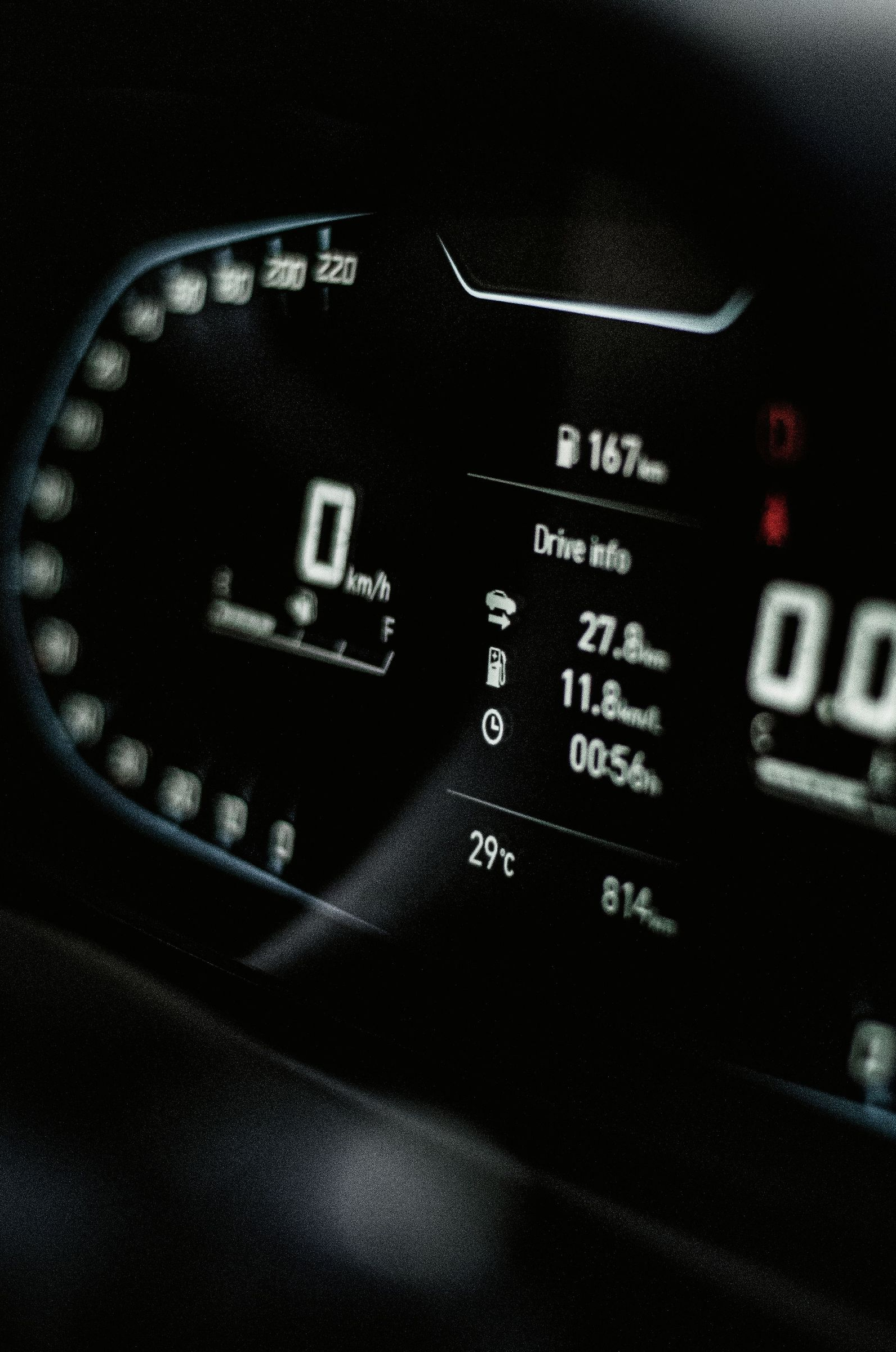 Car dashboard digital instrument cluster showing speed, fuel, and driving range at night
