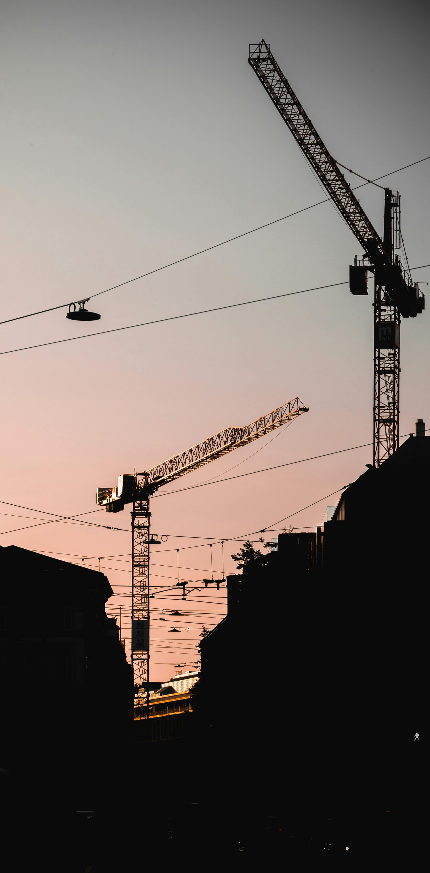 Silhouette of city skyline at sunset with three construction cranes.