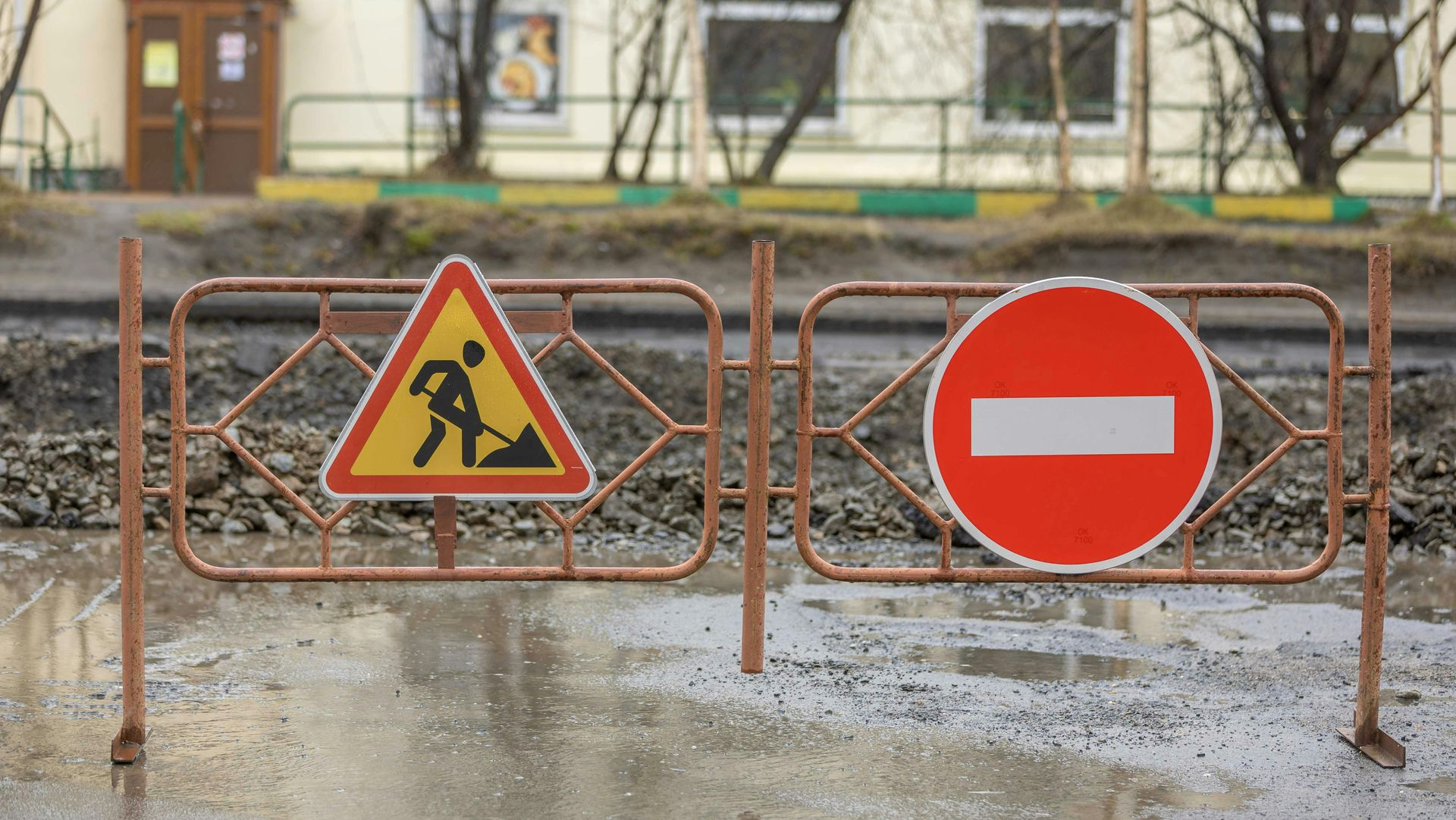 Roadworks barrier with warning signs and a no-entry sign on a wet street.