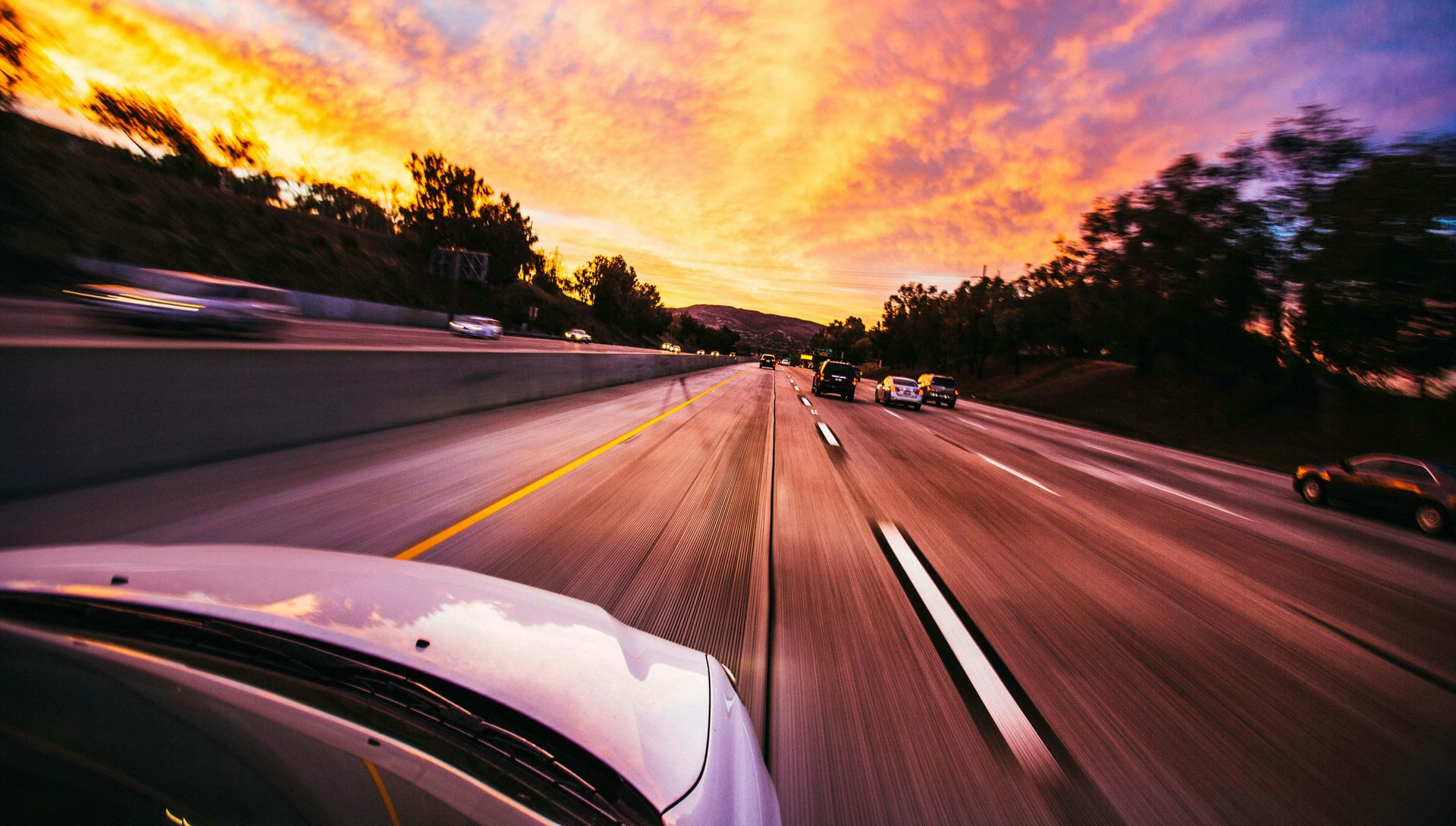 Highway with blurred cars under a vibrant sunset sky, orange and pink hues.