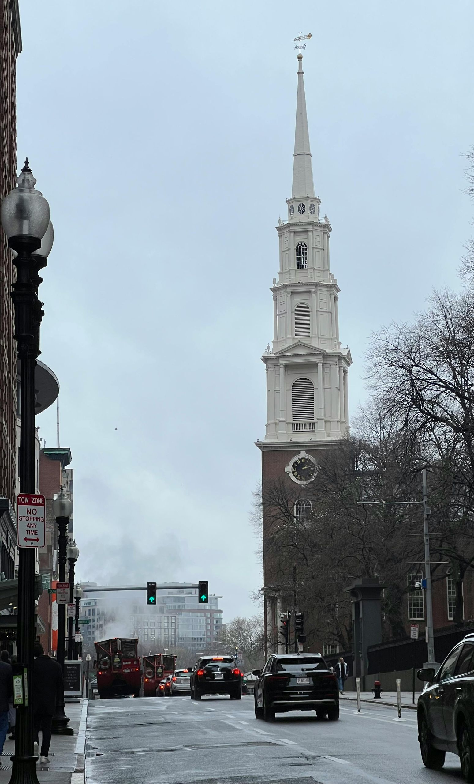 Street view of a church with a tall white steeple, cars on the street, and overcast sky.