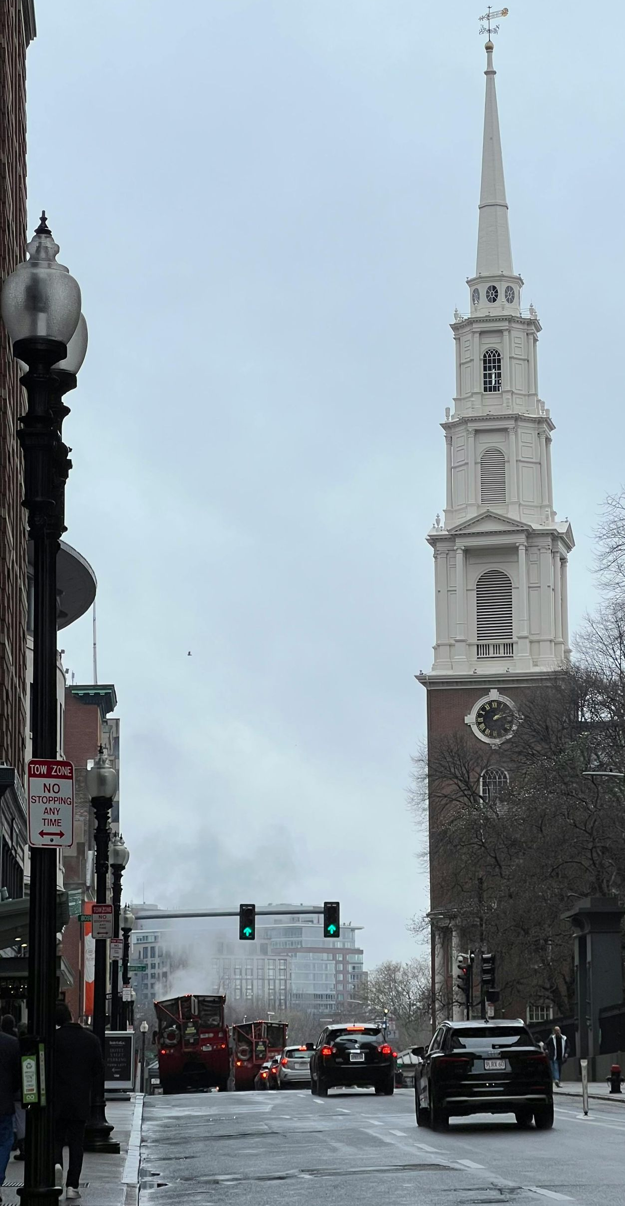 Street view of a church with a tall white steeple, cars on the street, and overcast sky.