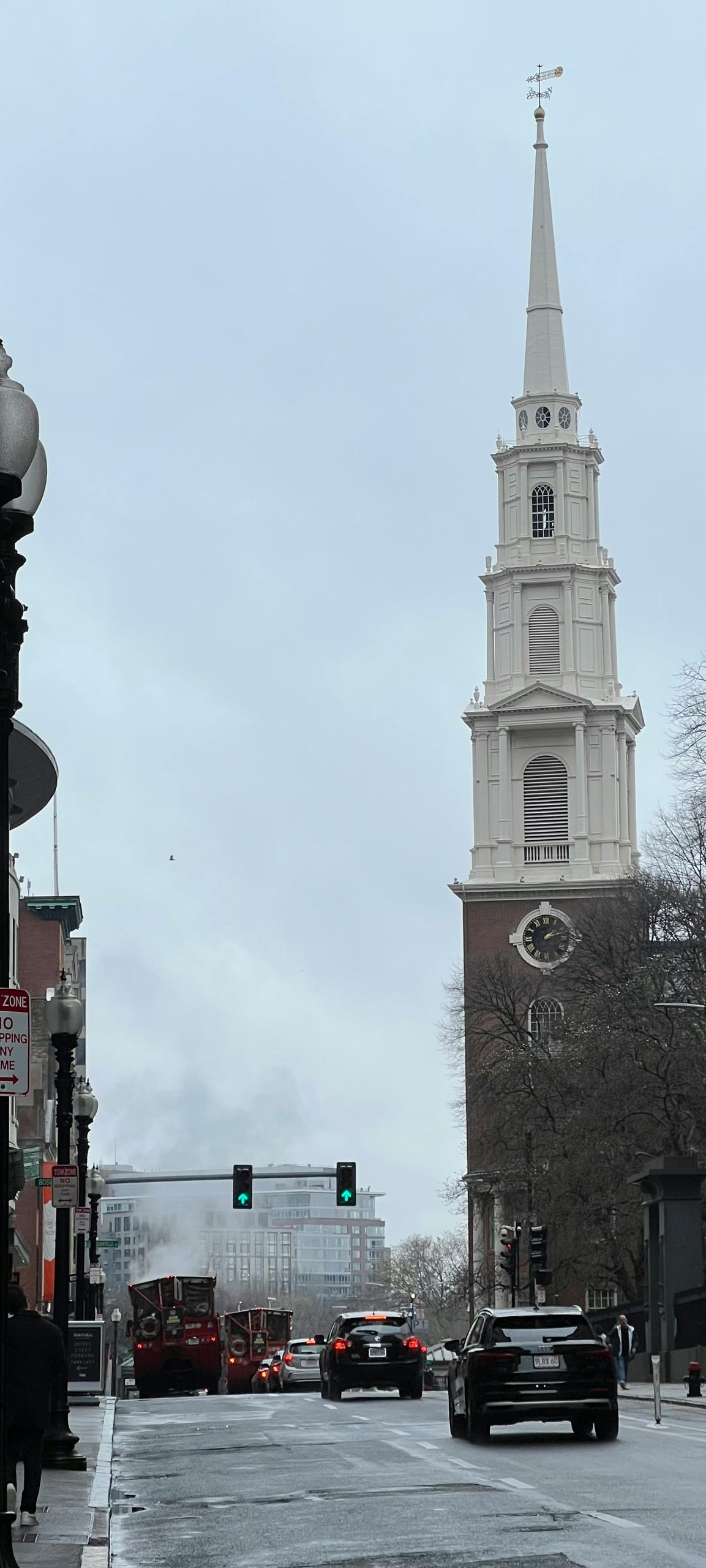 Street view of a church with a tall white steeple, cars on the street, and overcast sky.